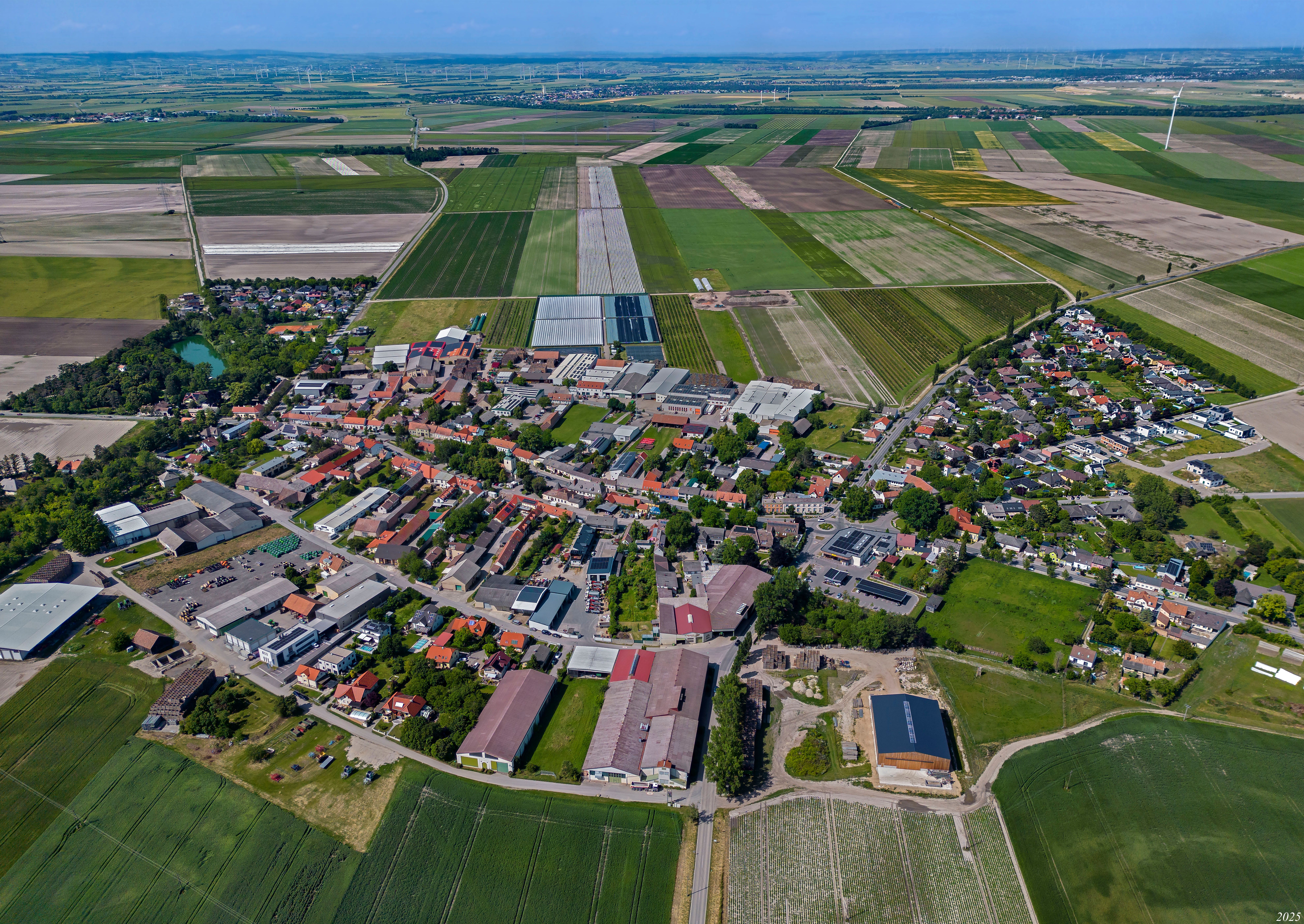 Raasdorf légi felvétele a település központjával, mezőkkel, üvegházakkal és a környéken található szélturbinákkal.