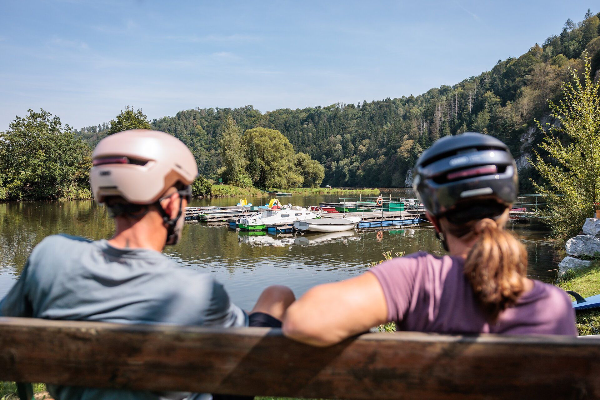 A lágy szellő simogatja a csillogó víztározót, miközben a kerékpárosok egy padon pihenve élvezik a festői tájat. Ez a buja zölddel és dombokkal körülvett hely arra hívogat, hogy lazítson és megtapasztalja a természet szépségét.