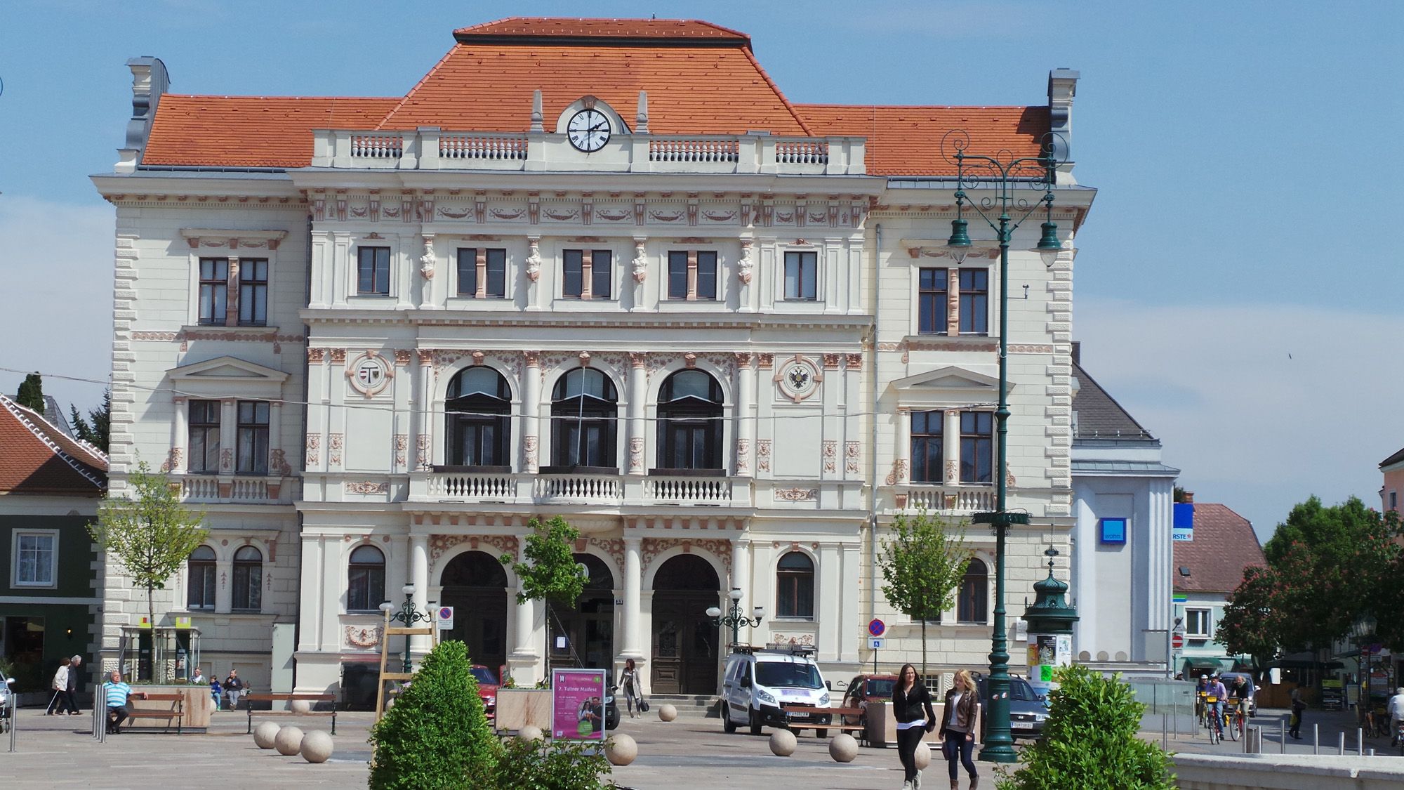 Historisches Gebäude mit Uhr und Verzierungen, Menschen und Autos im Vordergrund.