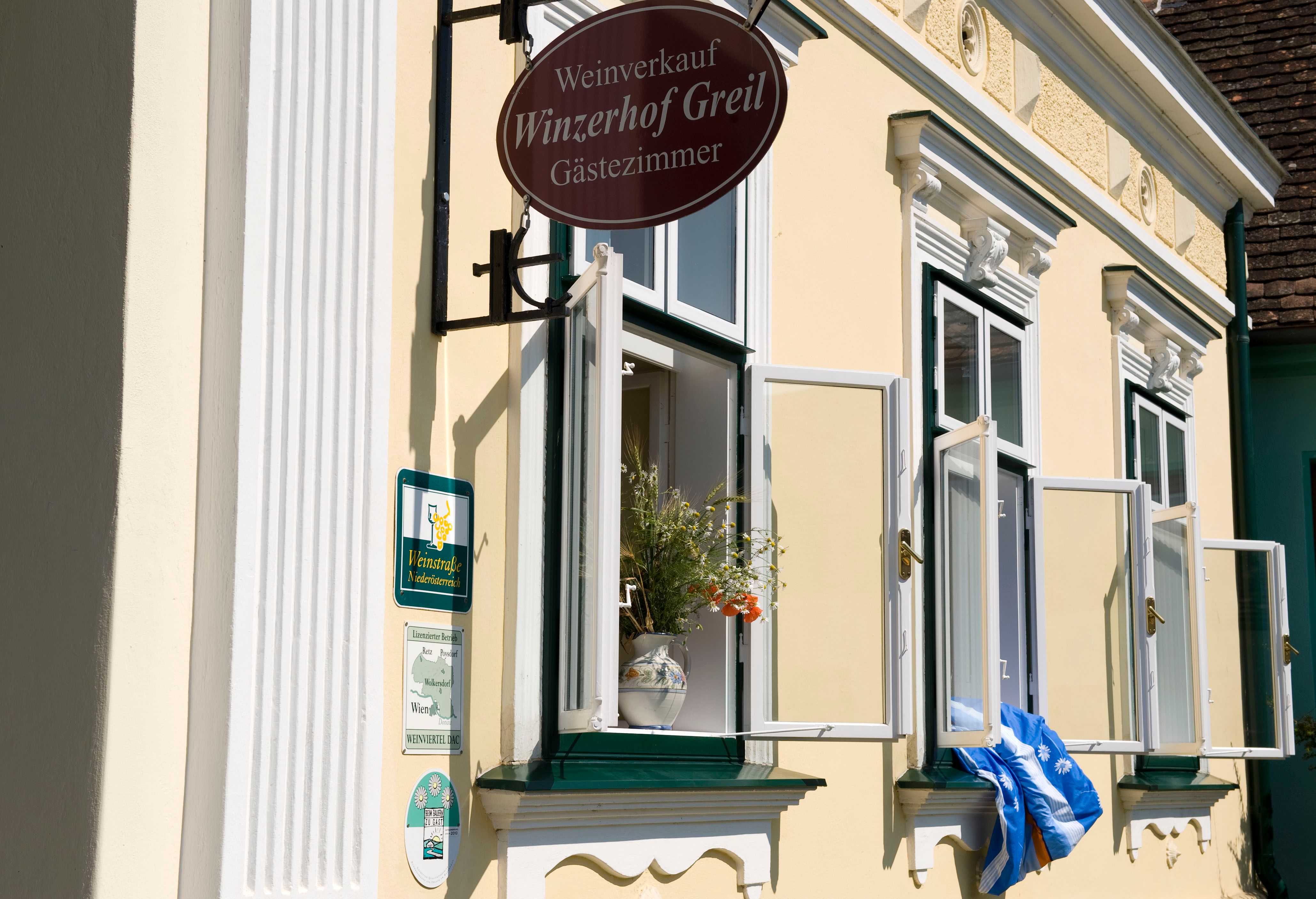 Egy sárga épület homlokzata nyitott ablakokkal és a "Winzerhof Greil" felirattal.