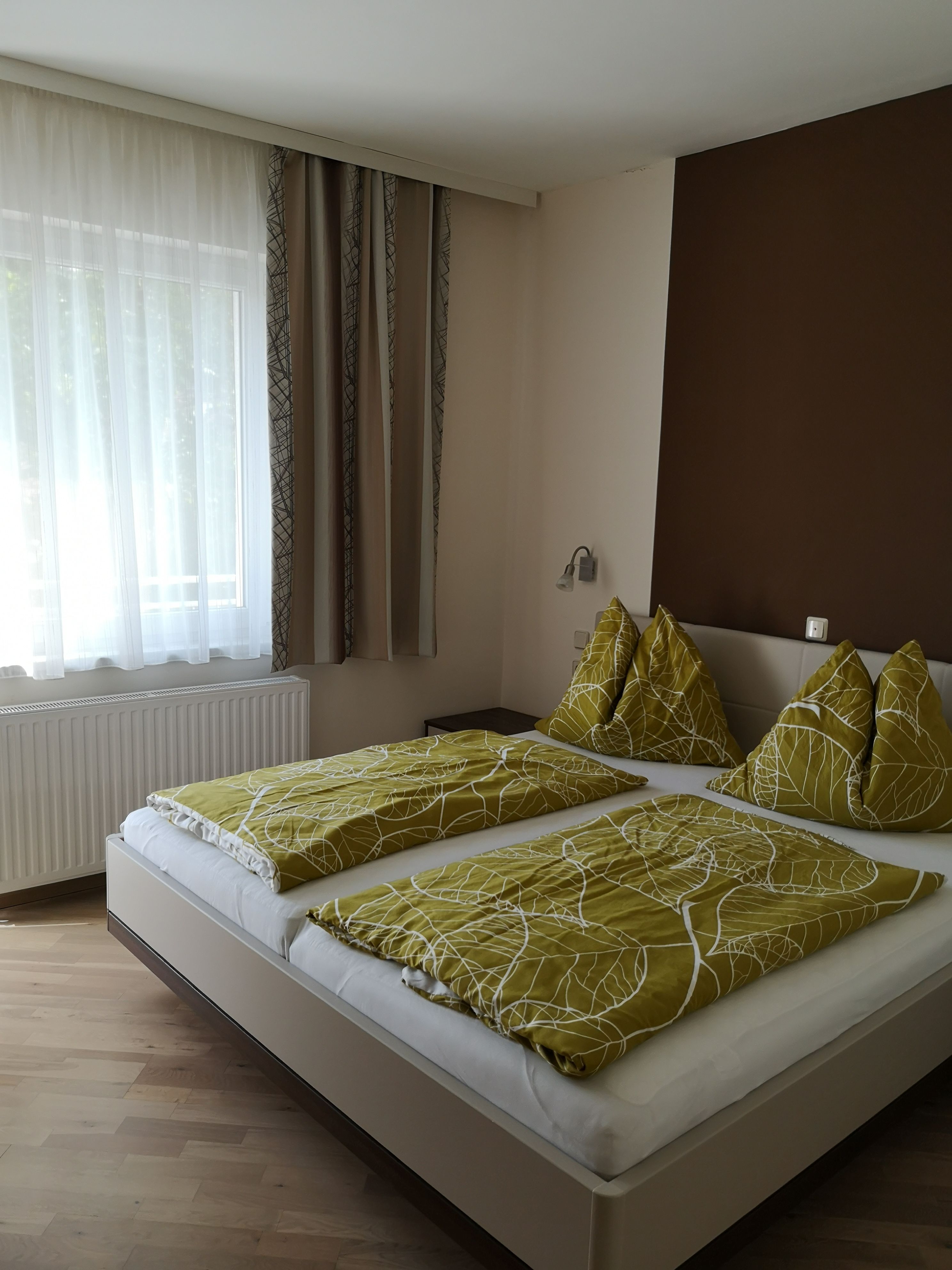 Kétágyas szoba egy ággyal, zöld ágyneművel és függönyös ablakkal.