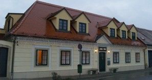 Kétszintes épület sárga homlokzattal és piros tetővel.