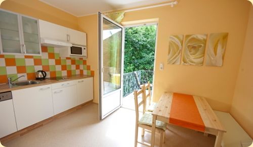 Világos konyha étkezővel, színes csempézett fröccsöntővel és nyitott erkélyajtóval.