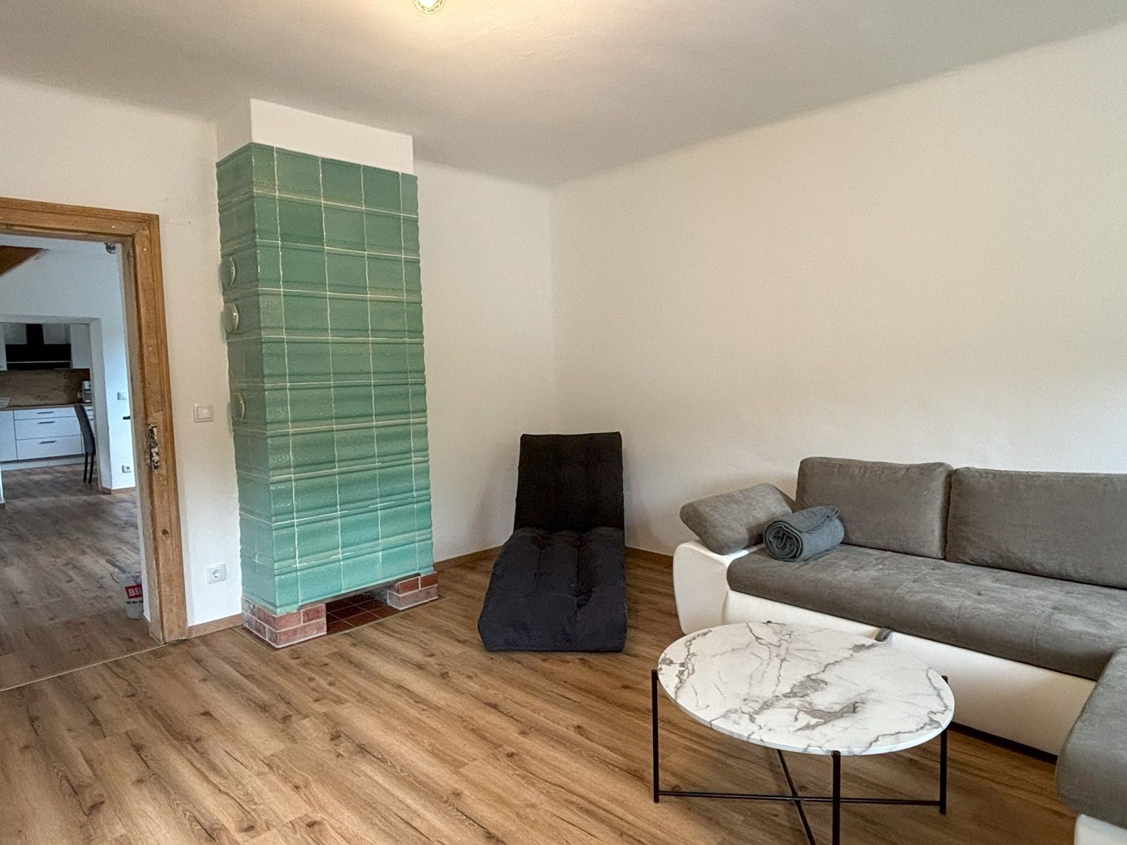 Nappali szürke kanapéval, kerek márványasztallal és zöld cserépkályhával.