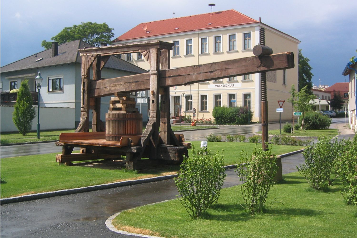 Történelmi fanyomda egy iskolaépület előtt zöld környezetben.