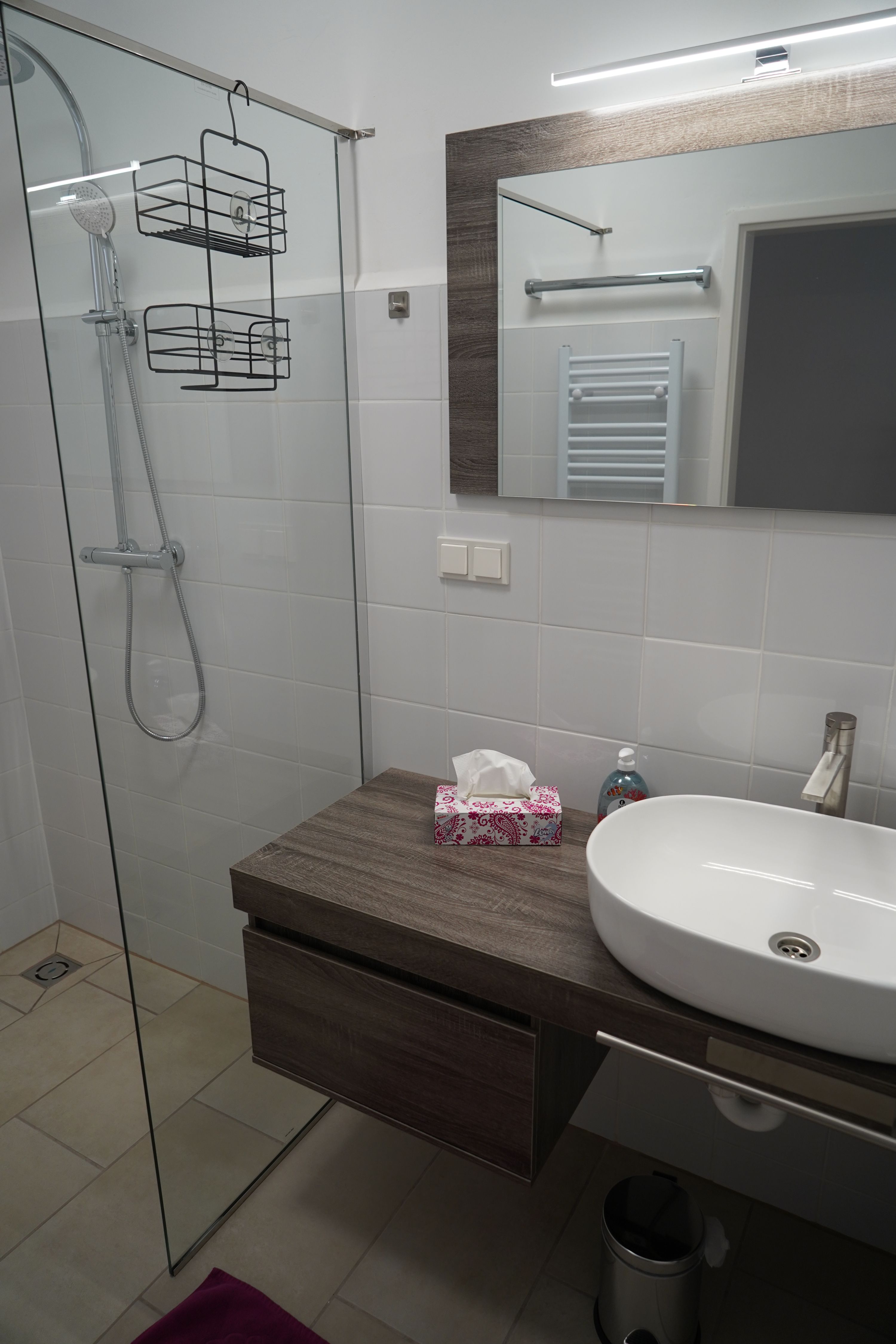 Modern fürdőszoba üvegzuhannyal, mosdókagylóval és tükörrel.