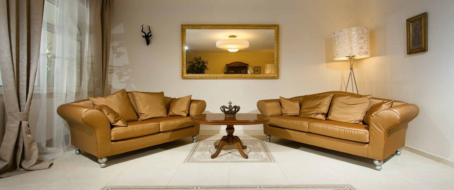 Elegáns lobby két barna kanapéval, egy kerek faasztallal és egy nagy tükörrel a falon.
