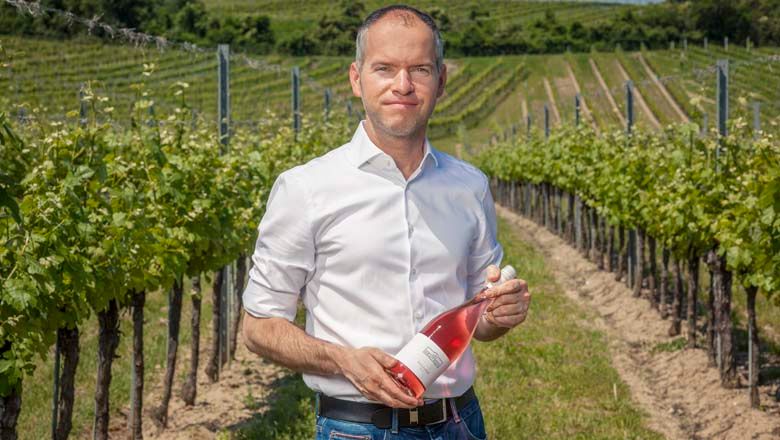 Férfi egy szőlőskertben, kezében egy üveg rozé borral.