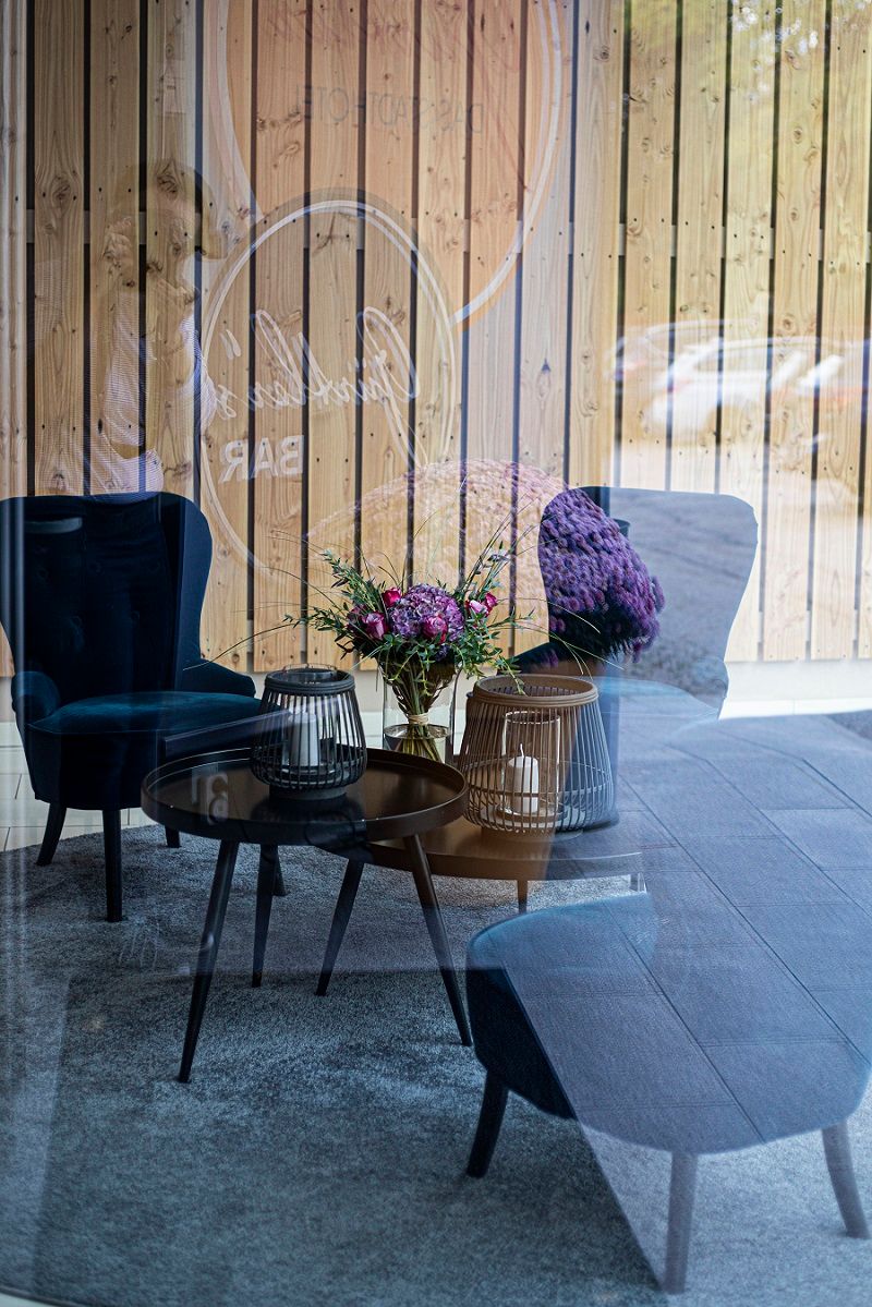 Hangulatos társalgó kék fotelekkel, gyertyás asztallal és egy üvegfalban tükröződő virágcsokorral.