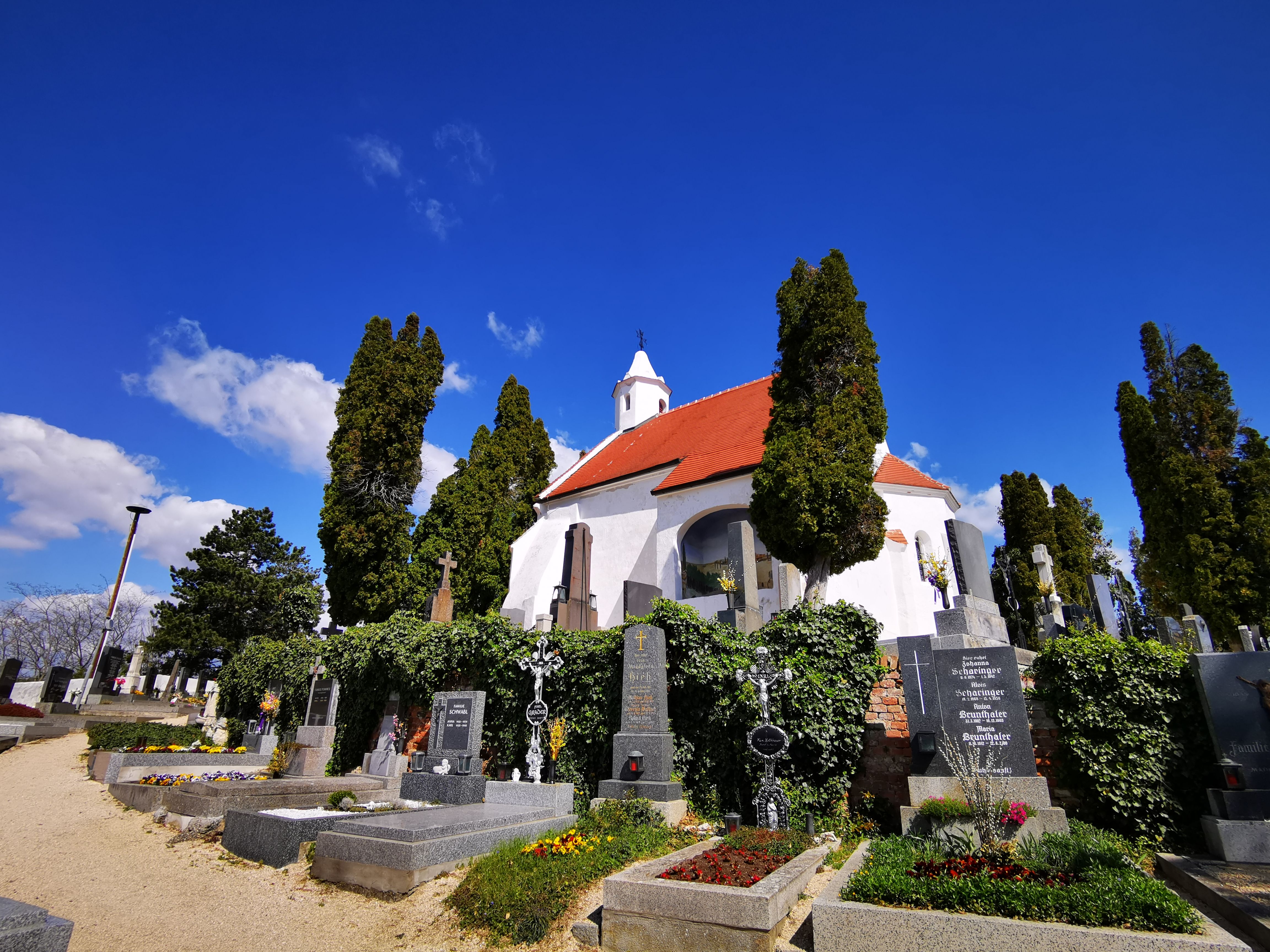 Kunigungenkirche templom Mailbergben, előtérben temető és virágzó sírok.