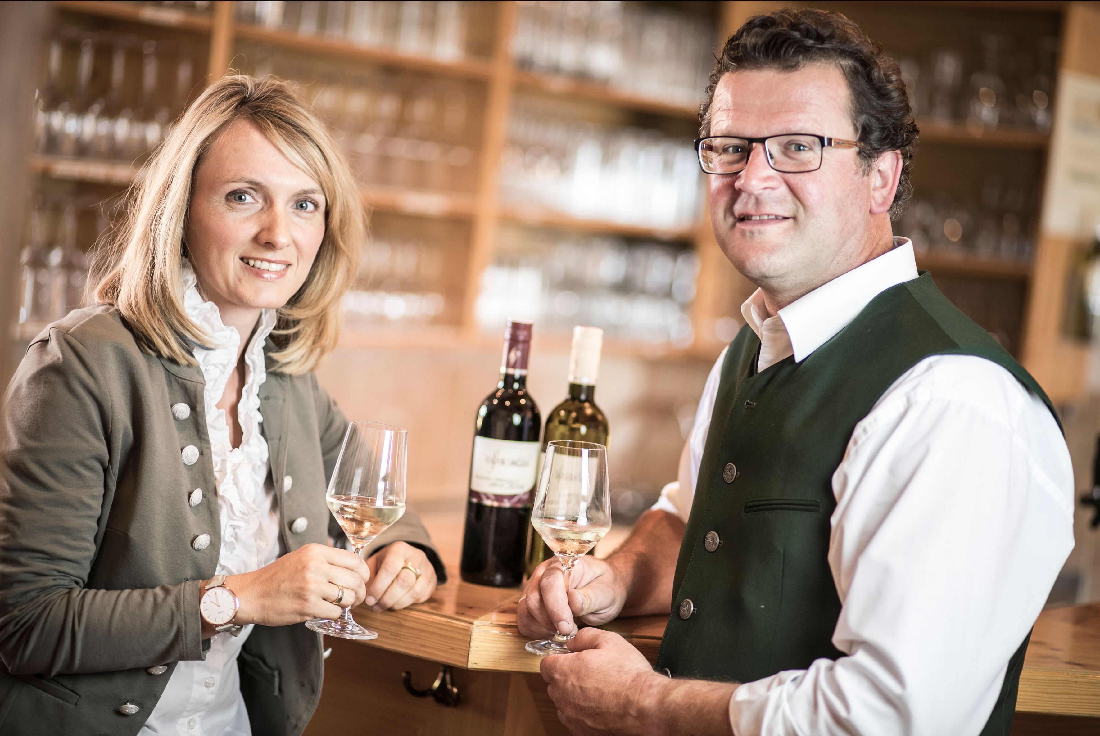 Két hagyományos öltözetű ember borospoharat tart egy borozóban.