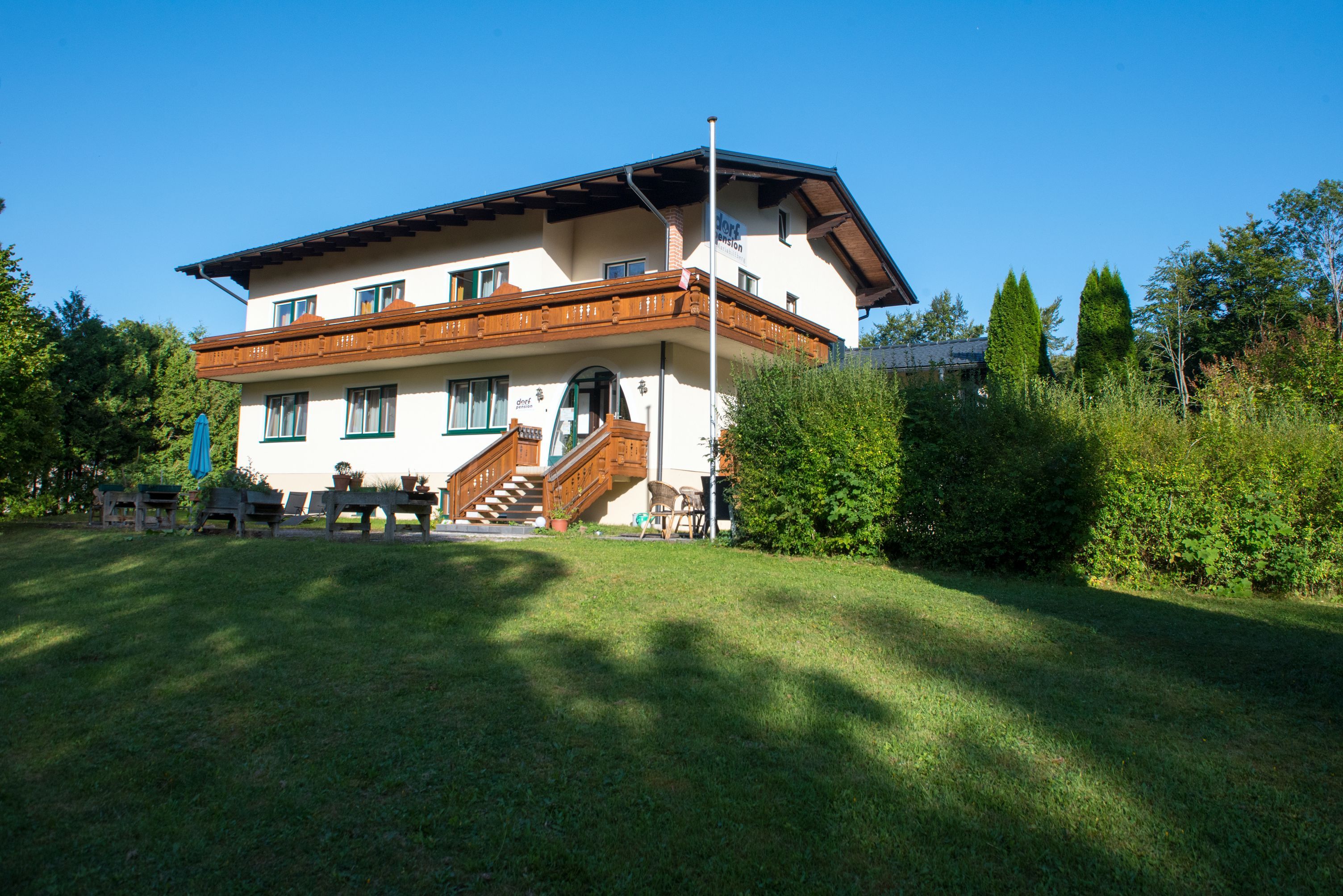 Kétszintes ház fából készült verandával és kerttel.