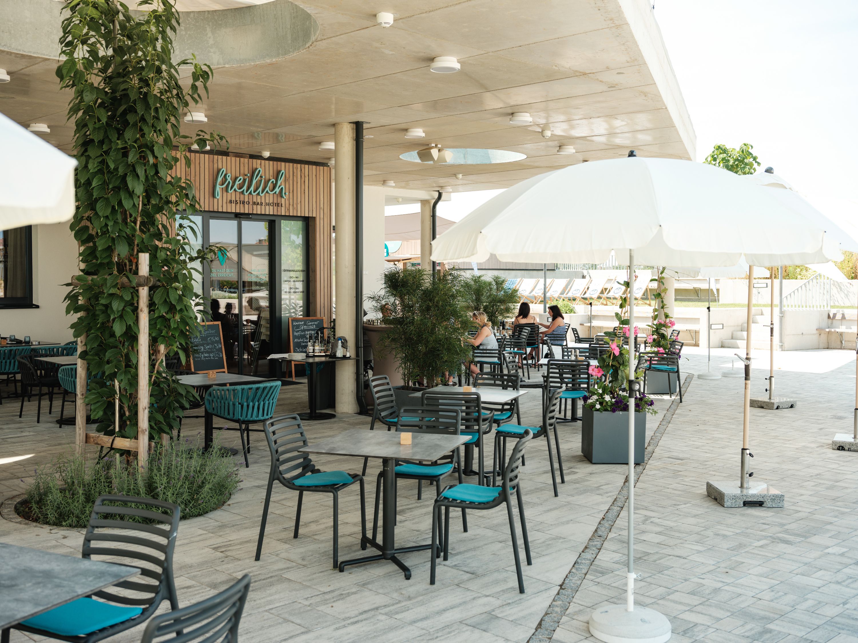 Egy kávézó szabadtéri területe asztalokkal, székekkel és napernyőkkel.