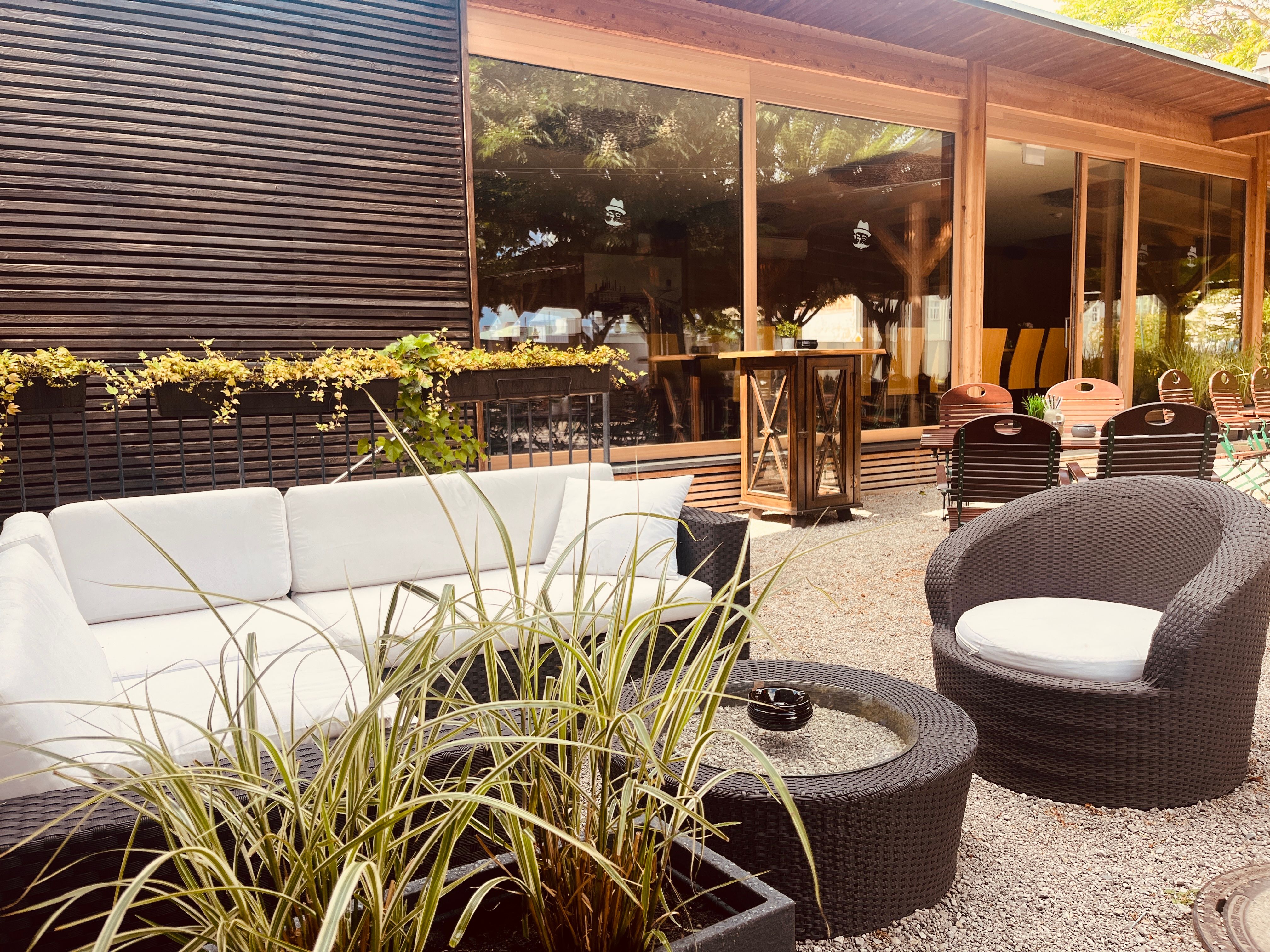 Hangulatos szabadtéri társalgó fehér kanapékkal, kerek asztalokkal és növényekkel.