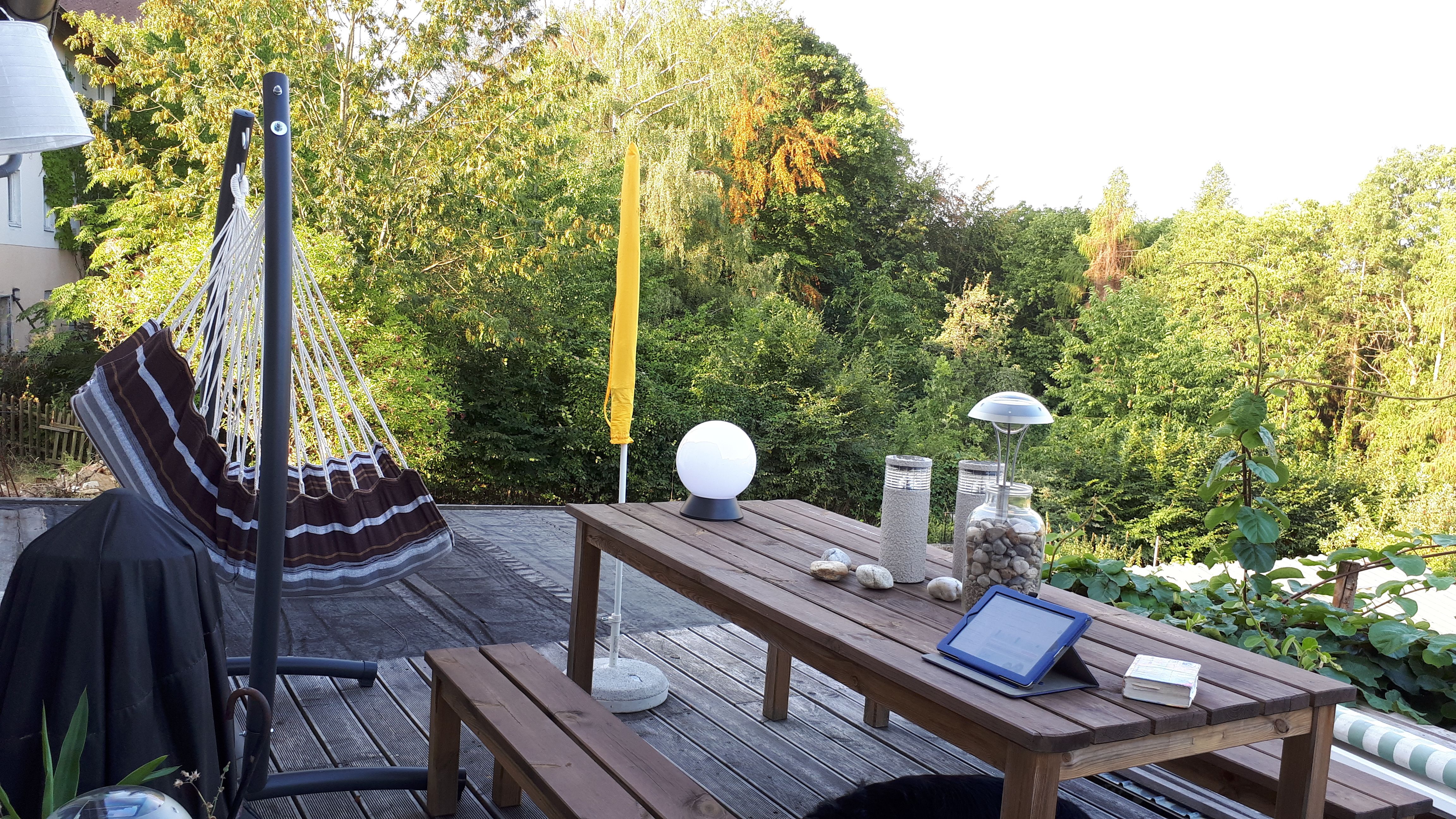 Terasz függőággyal, fa asztallal és kilátással a zöld fákra.