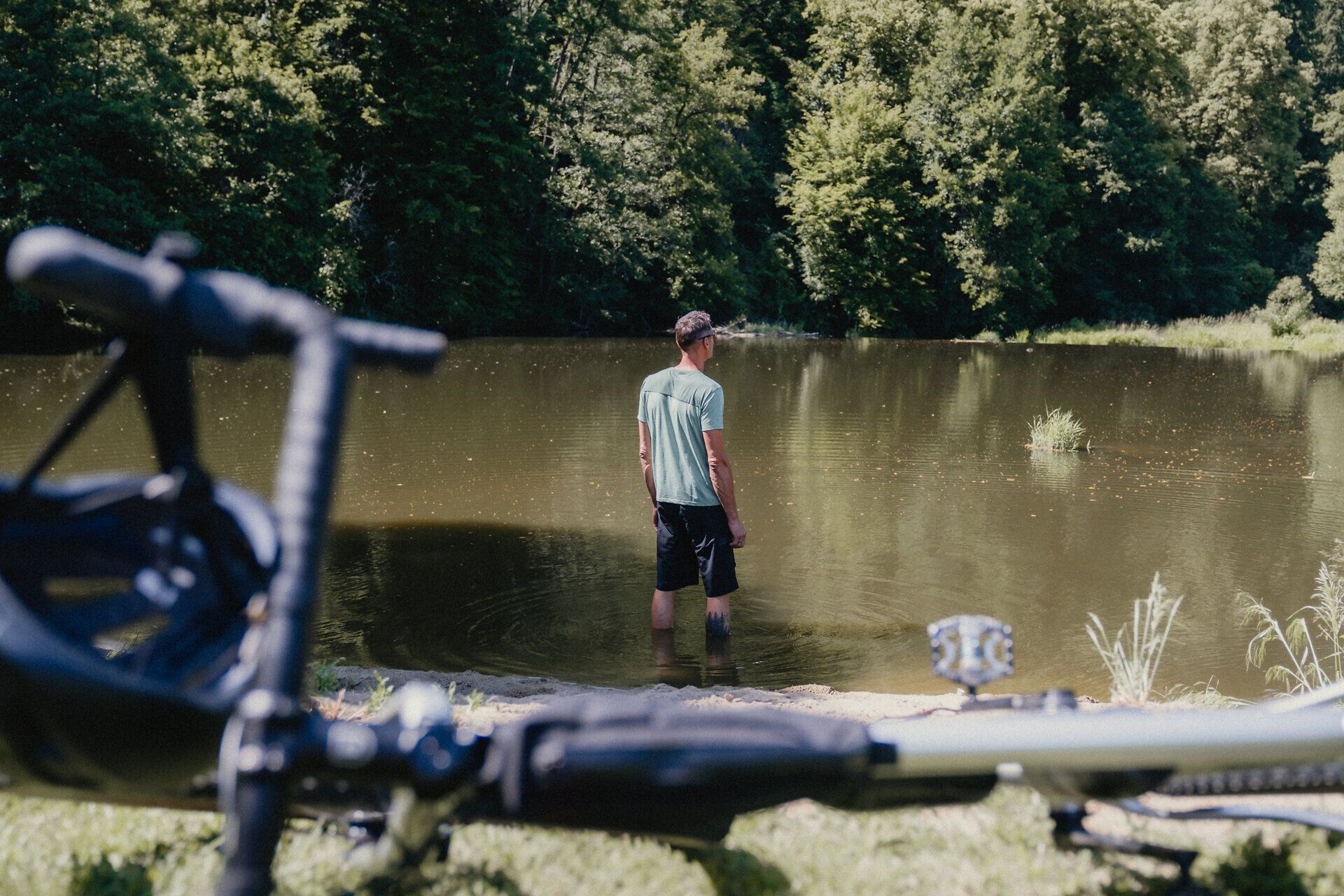 Ein Mann in Sportkleidung steht im Strandbad und blickt in die Ferne, im Vordergrund ist ein Rad angeschnitten