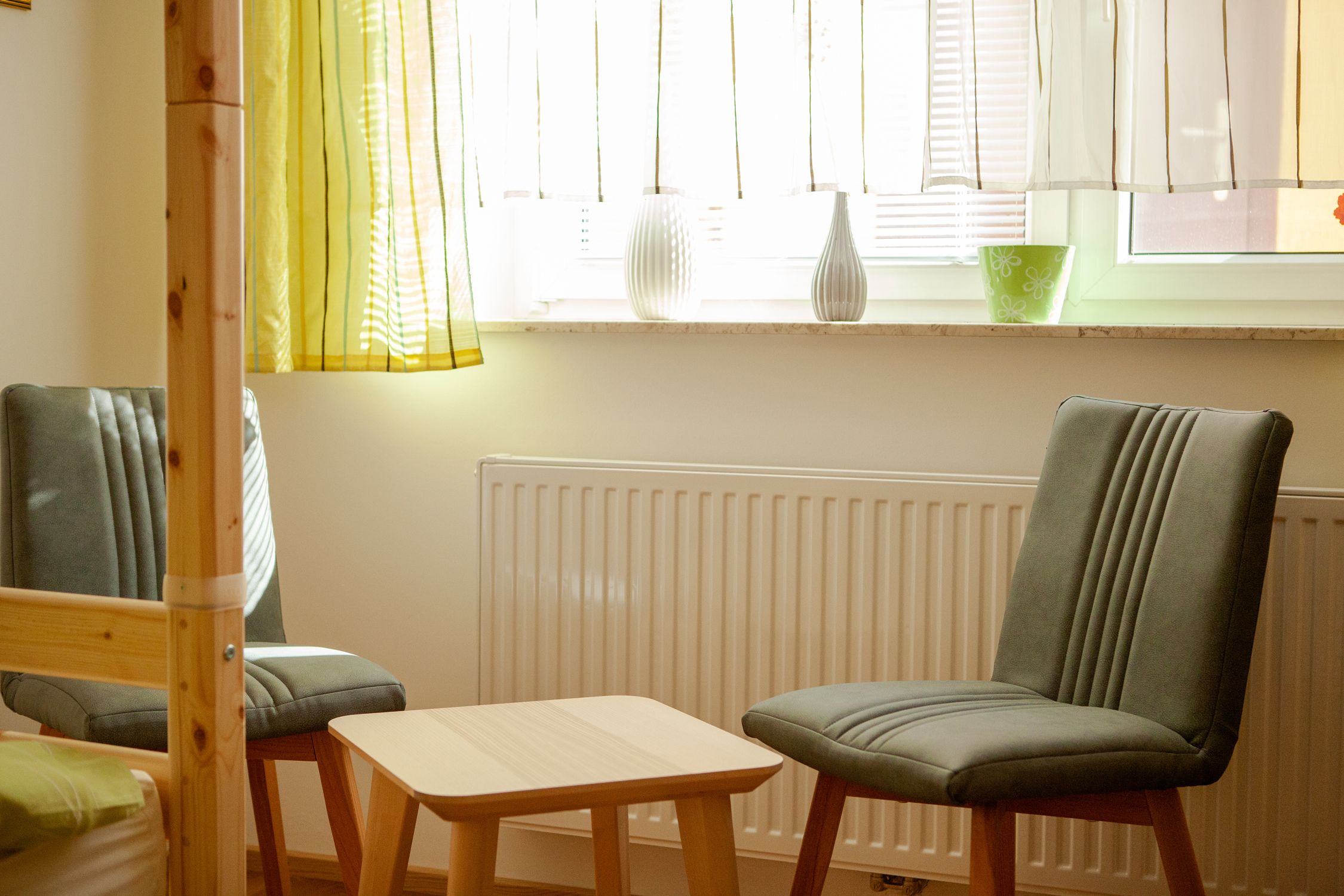 Két szürke szék és egy kis faasztal a hálószoba függönyös ablaka előtt.