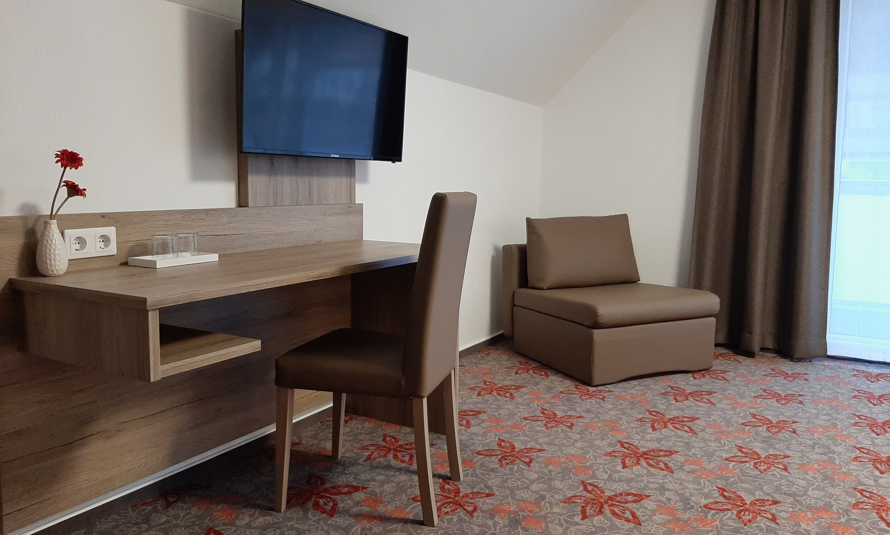 Hotelszoba íróasztallal, székkel, televízióval és karosszékkel.