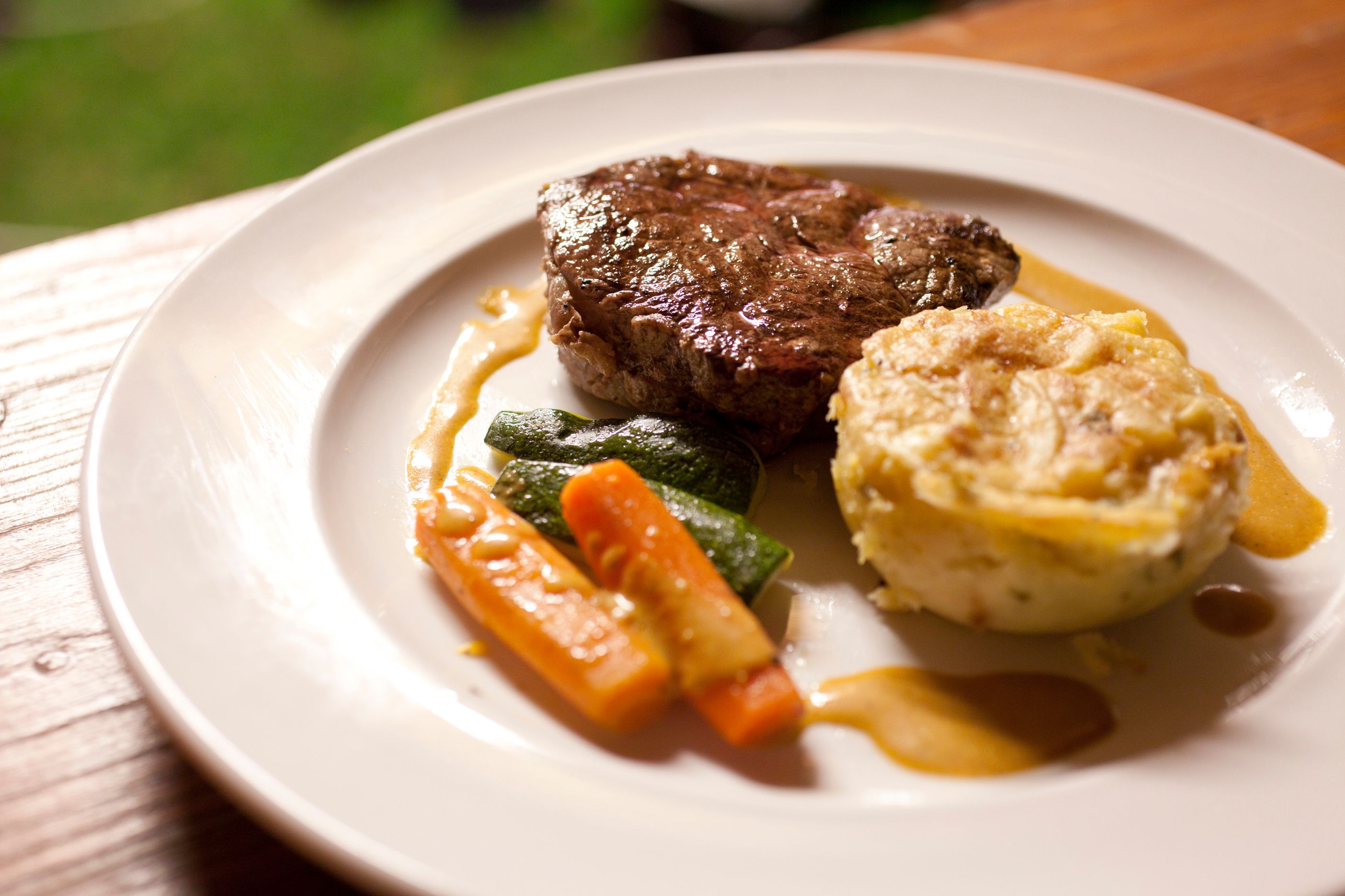 Egy tányér egy szelet hússal, zöldségekkel és burgonyagratinnal.