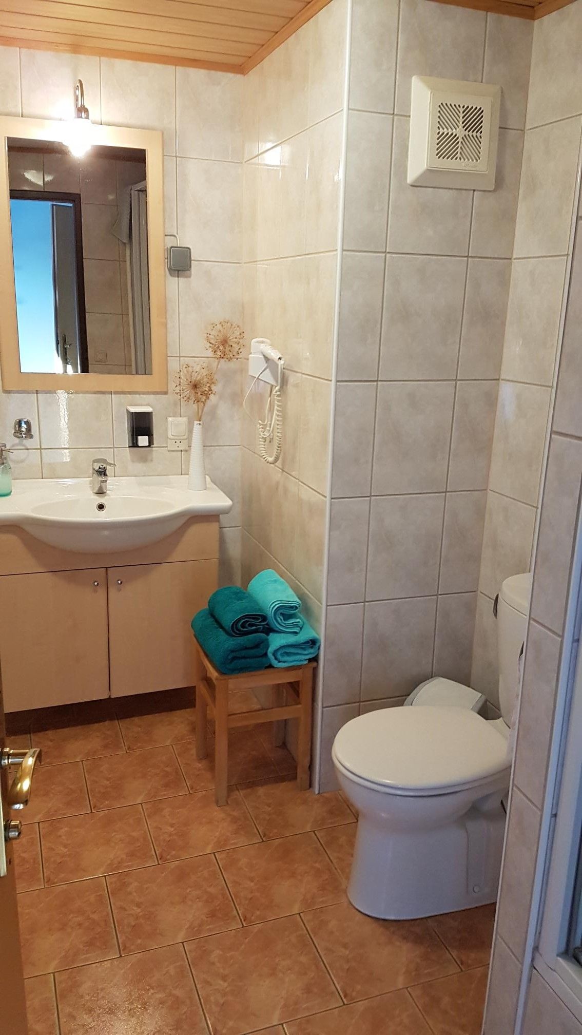 Fürdőszoba mosdóval, tükörrel, WC-vel és törölközőkkel egy zsámolyon.
