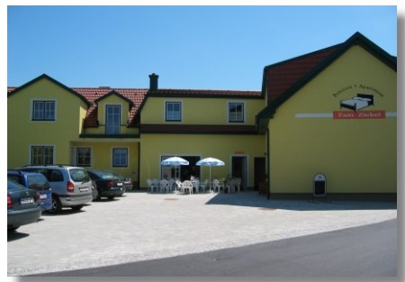 "Pension Ziekel" felirat&uacute; s&aacute;rga &eacute;p&uuml;let, előtte aut&oacute;k &eacute;s napernyős asztalok.