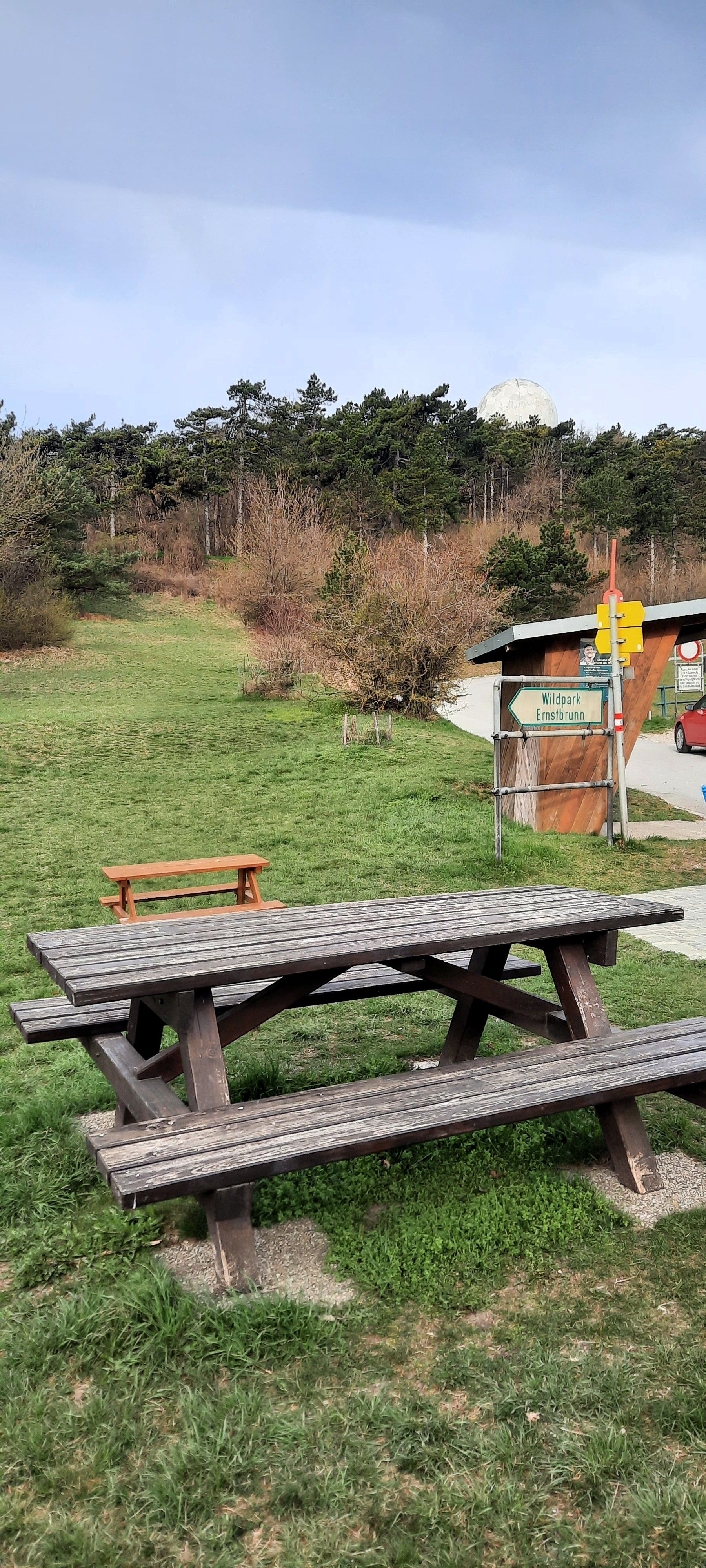 Piknikasztal egy réten, a háttérben erdővel és az Ernstbrunn Vadaspark táblájával.