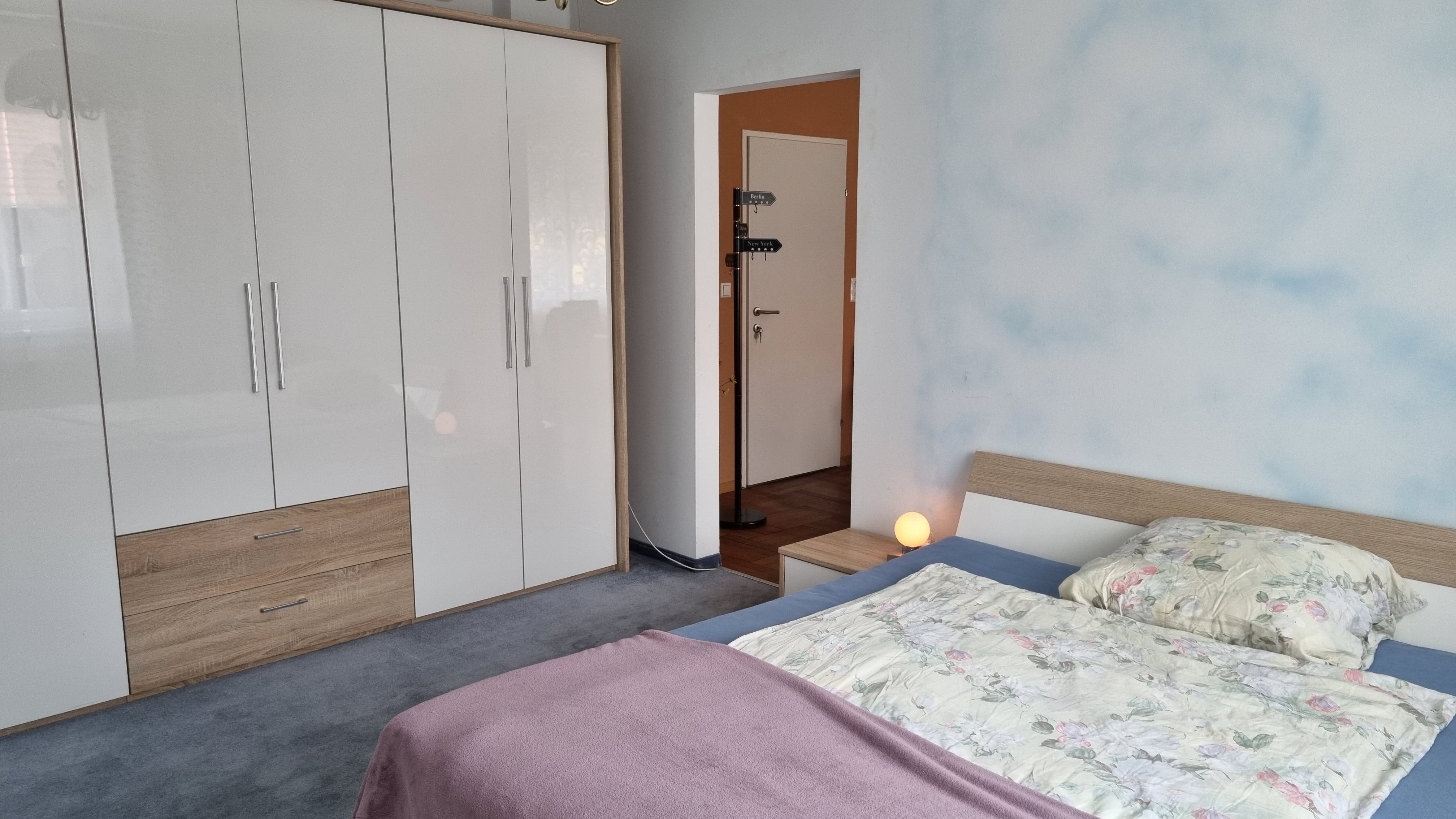 Egy hálószoba franciaággyal, nagy fehér szekrénnyel és éjjeli lámpával.