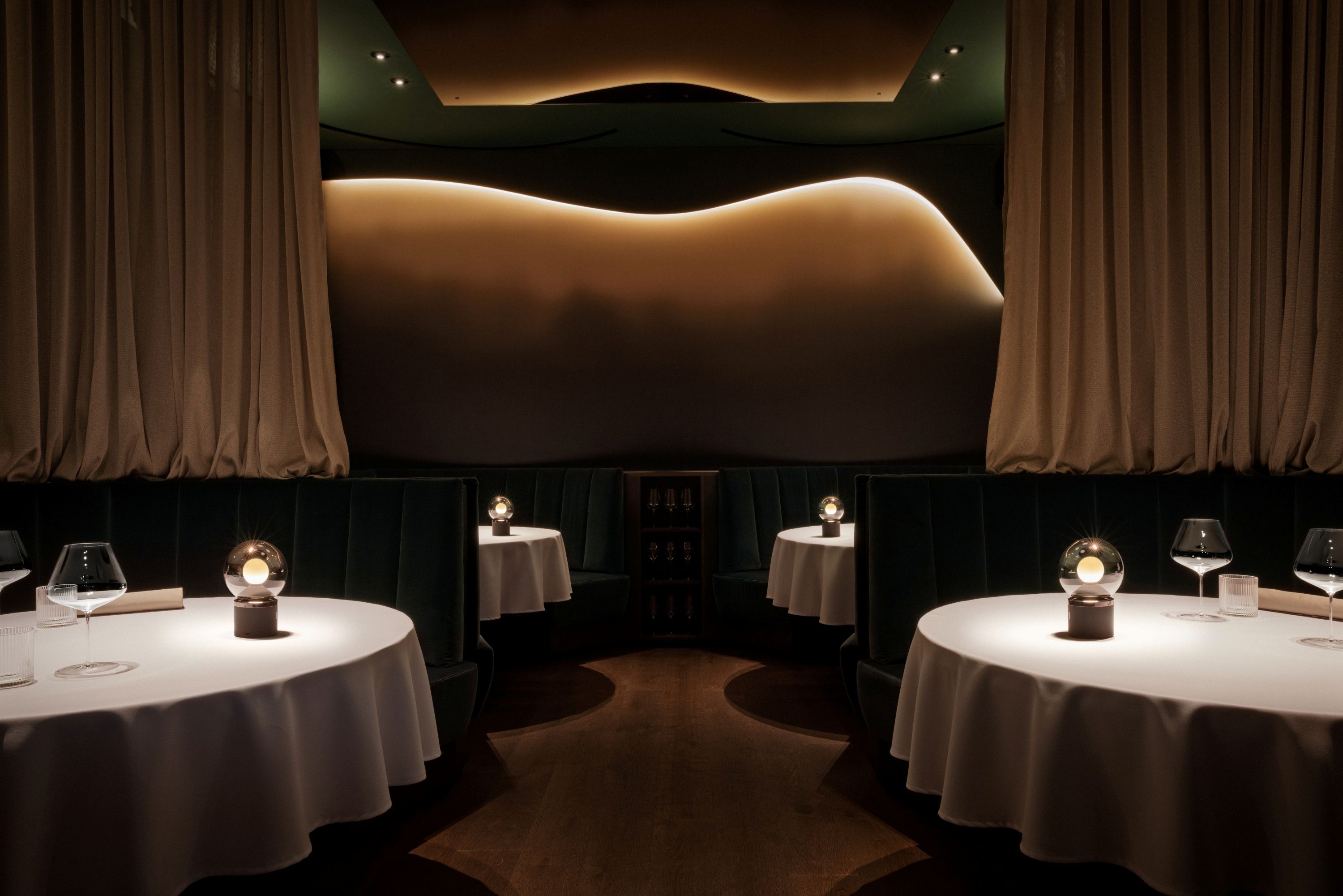 Elegáns étterem kerek asztalokkal, fehér terítőkkel és visszafogott világítással.
