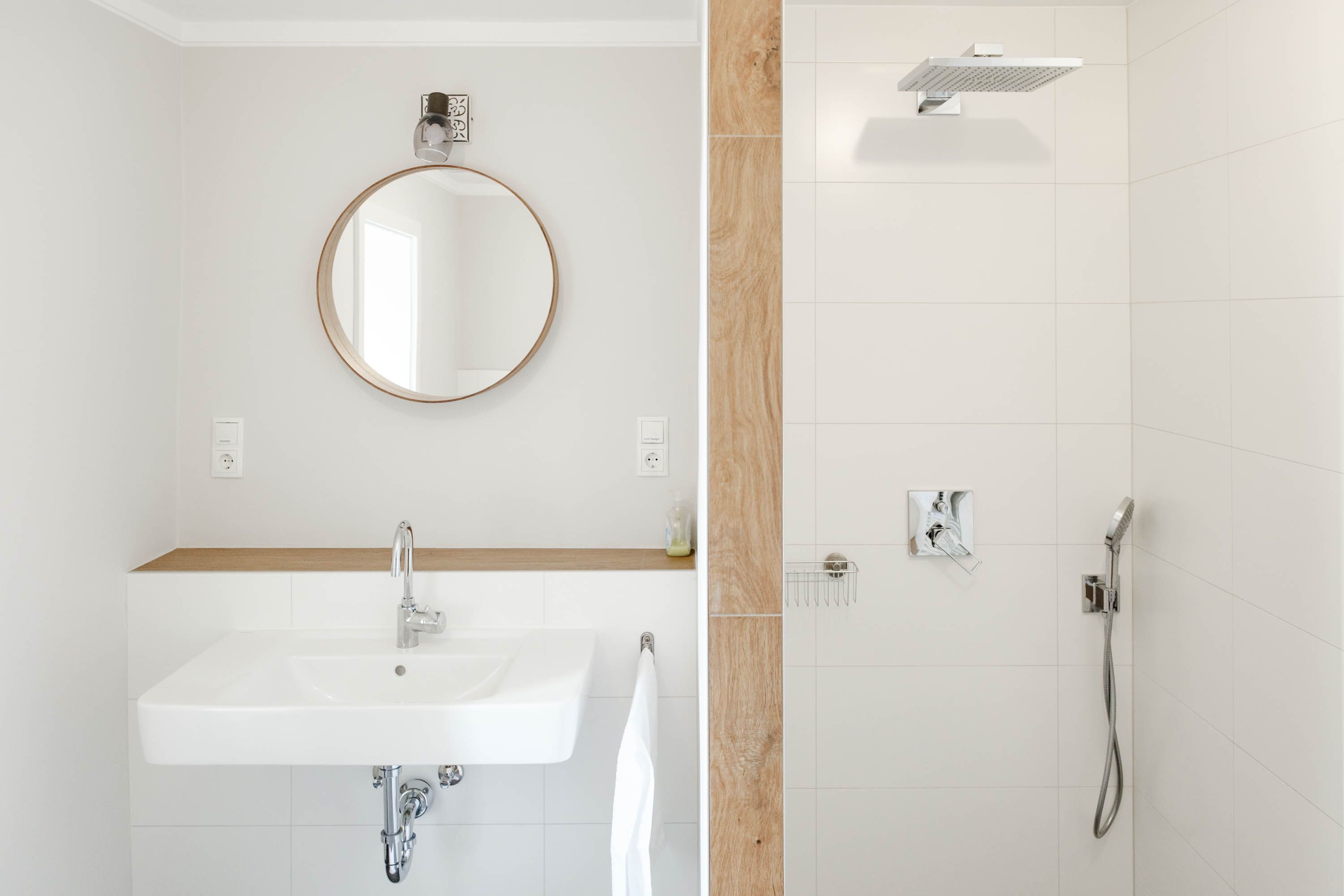 Modern fürdőszoba kerek tükörrel, mosdóval és zuhanyzóval.