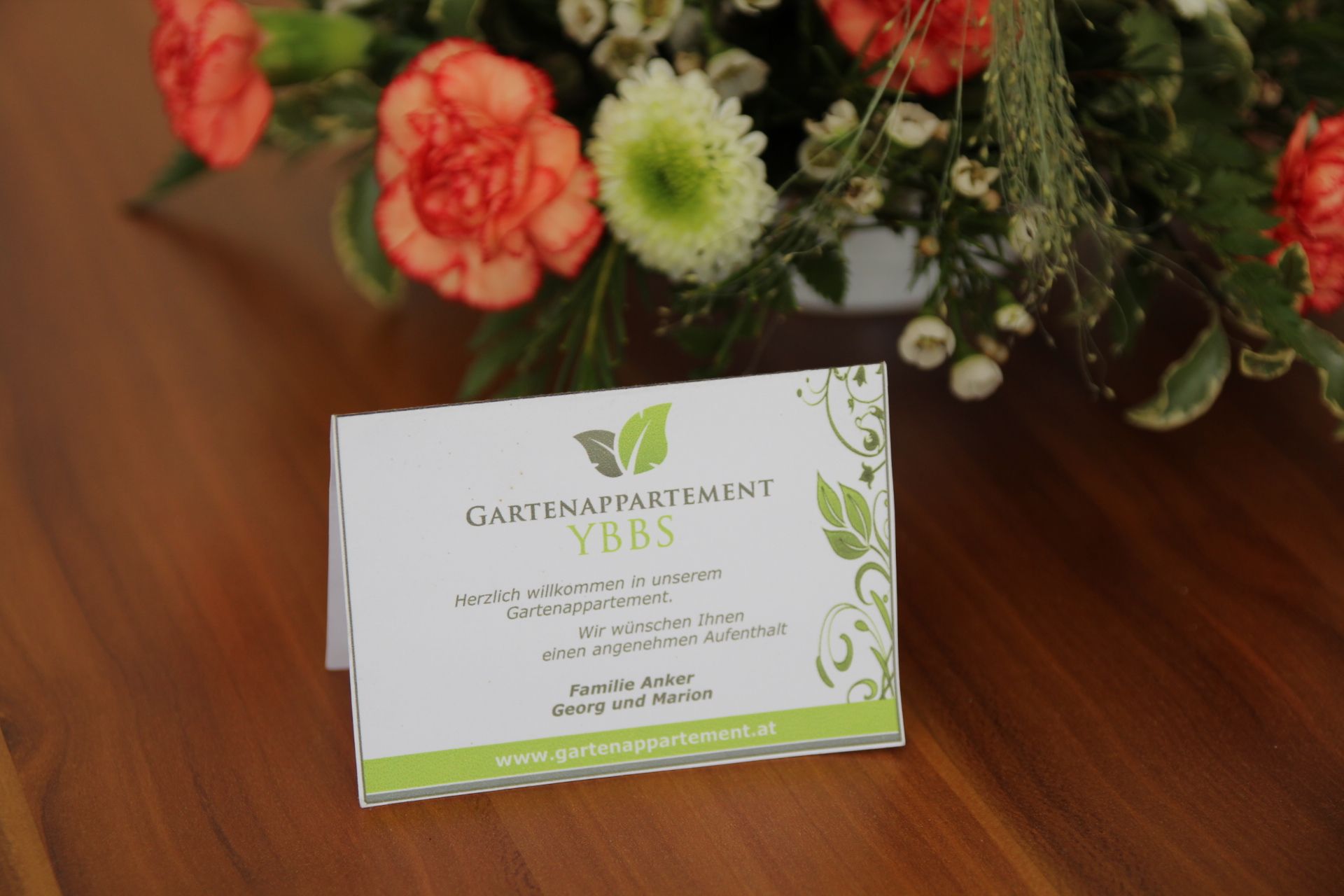 A Gartenappartement Ybbs üdvözlőlapja egy virágokkal díszített asztalon.