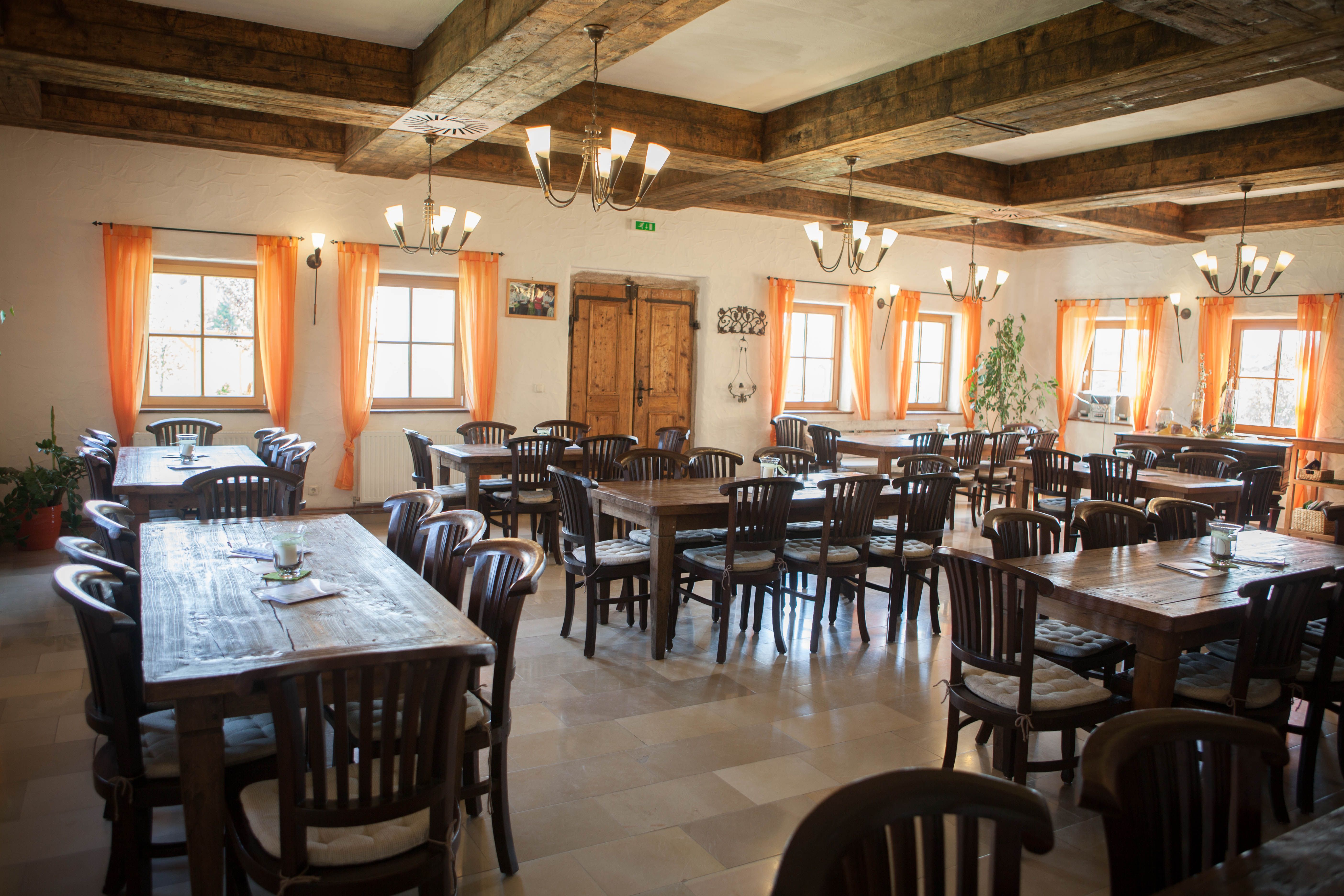 Rusztikus étkező, fa asztalokkal és székekkel, narancssárga függönyökkel és fagerendás mennyezettel.