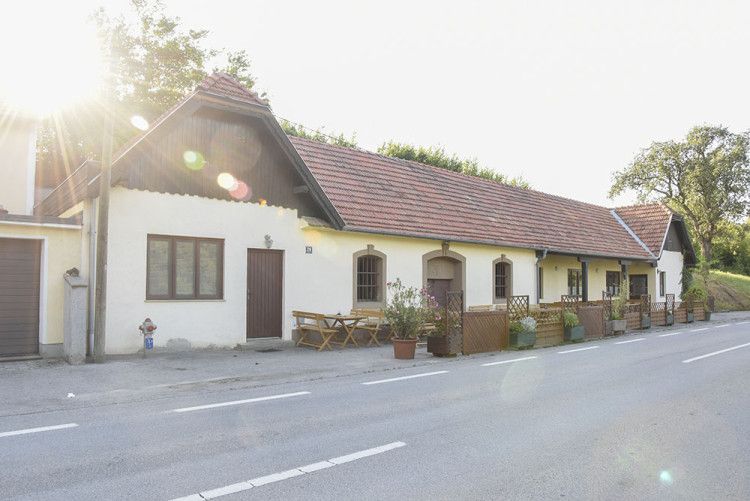 Hagyományos épület, vörös cseréptetővel és faasztalokkal az ajtó előtt, amelyet megvilágít a nap.
