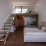 Modern szállodai szoba lépcsővel a félemeletre, franciaággyal és üvegfallal a fürdőszobába.
