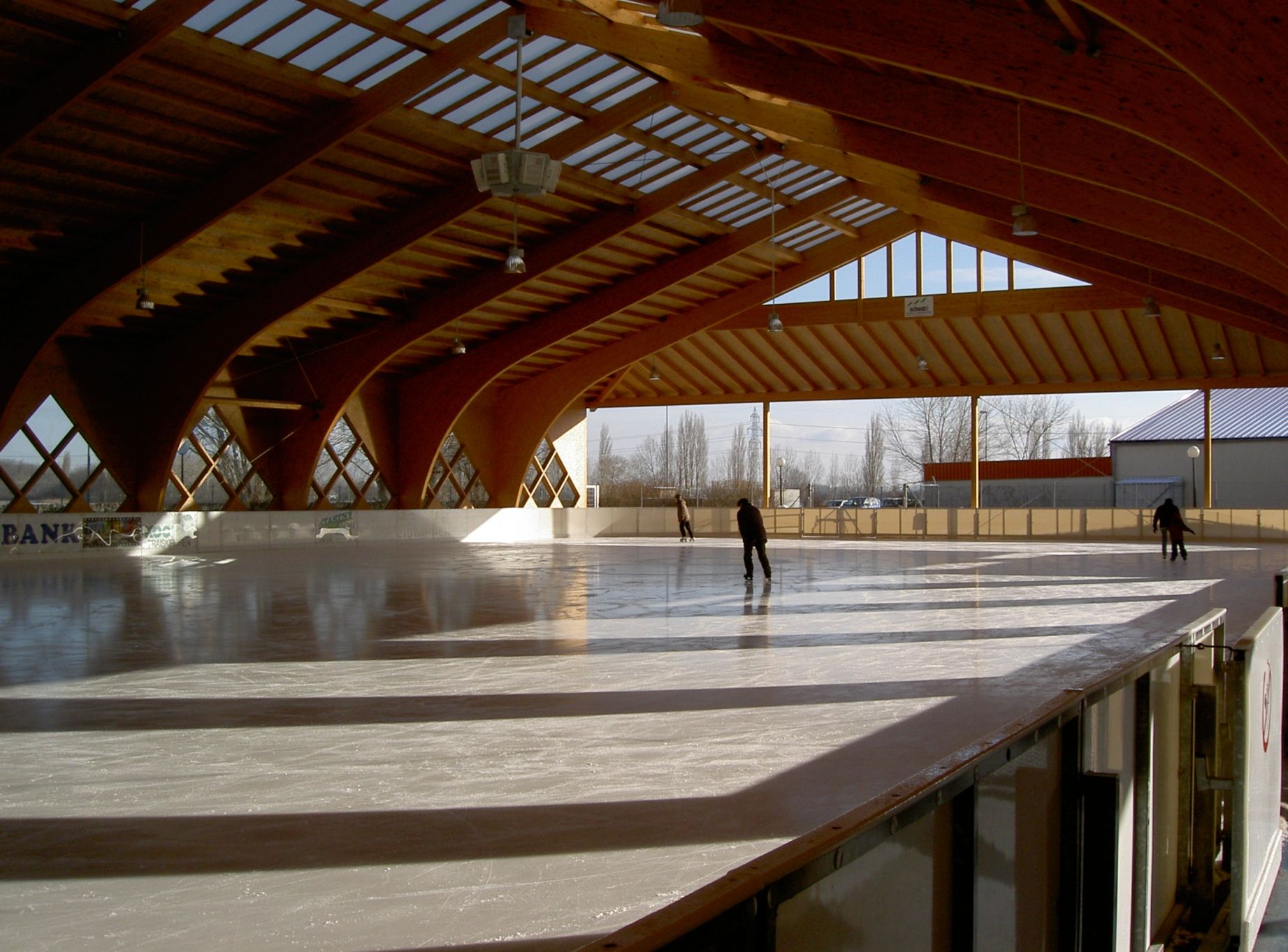 Fedett műjégpálya fából készült szerkezettel és korcsolyázókkal.