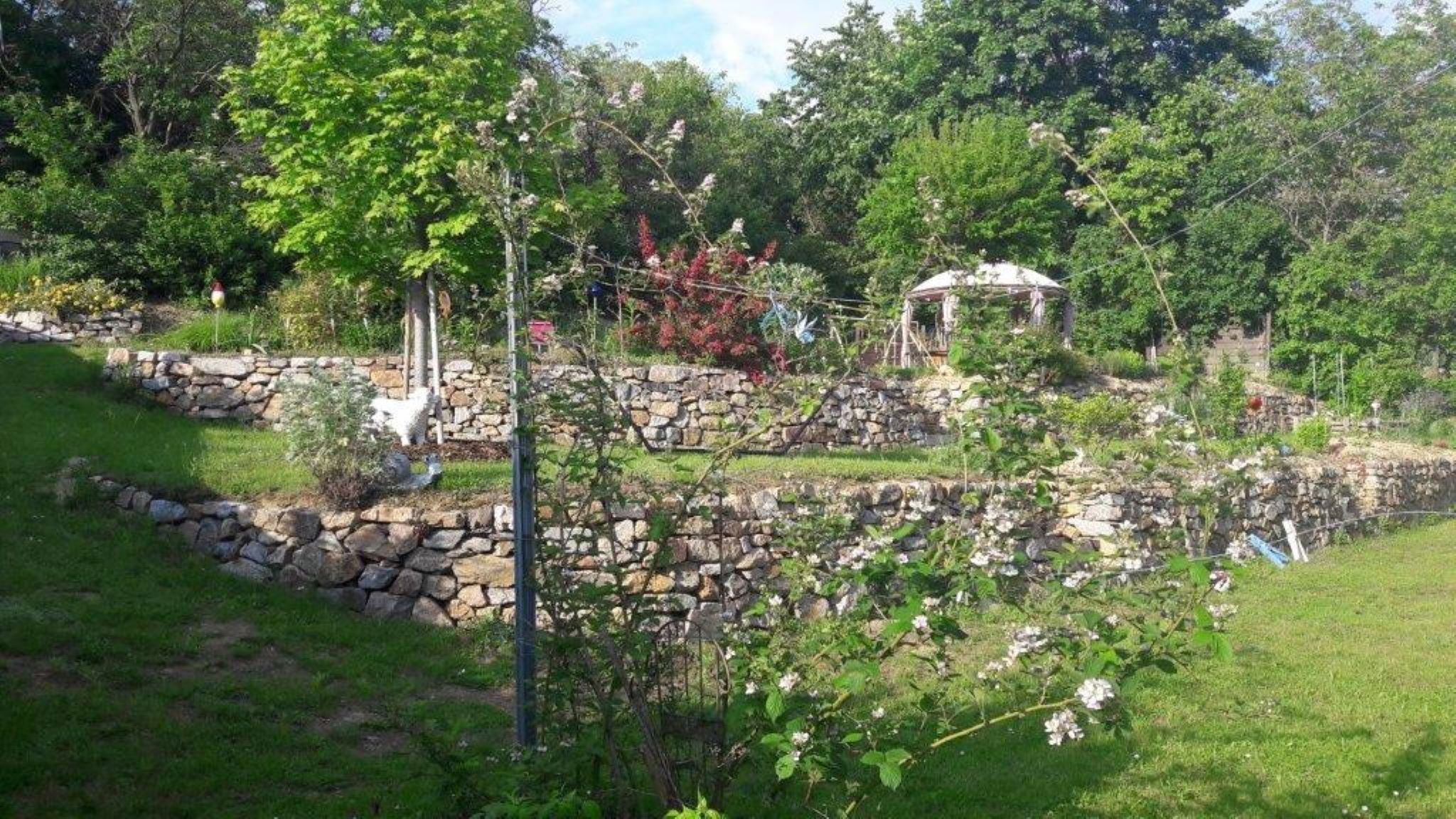Teraszos kert kőfalakkal és pavilonnal.