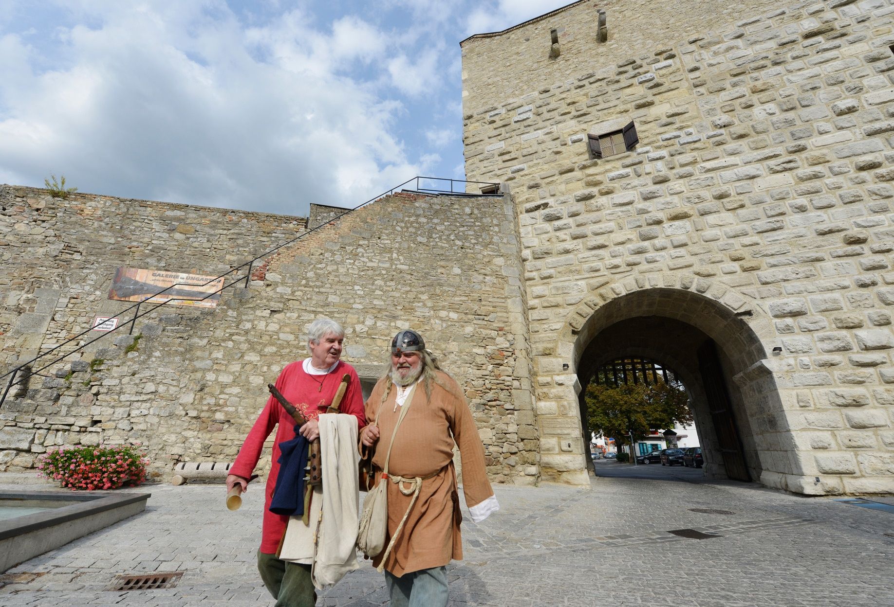 Két középkori ruhás férfi egy régi kőfal előtt Hainburg an der Donau-ban.