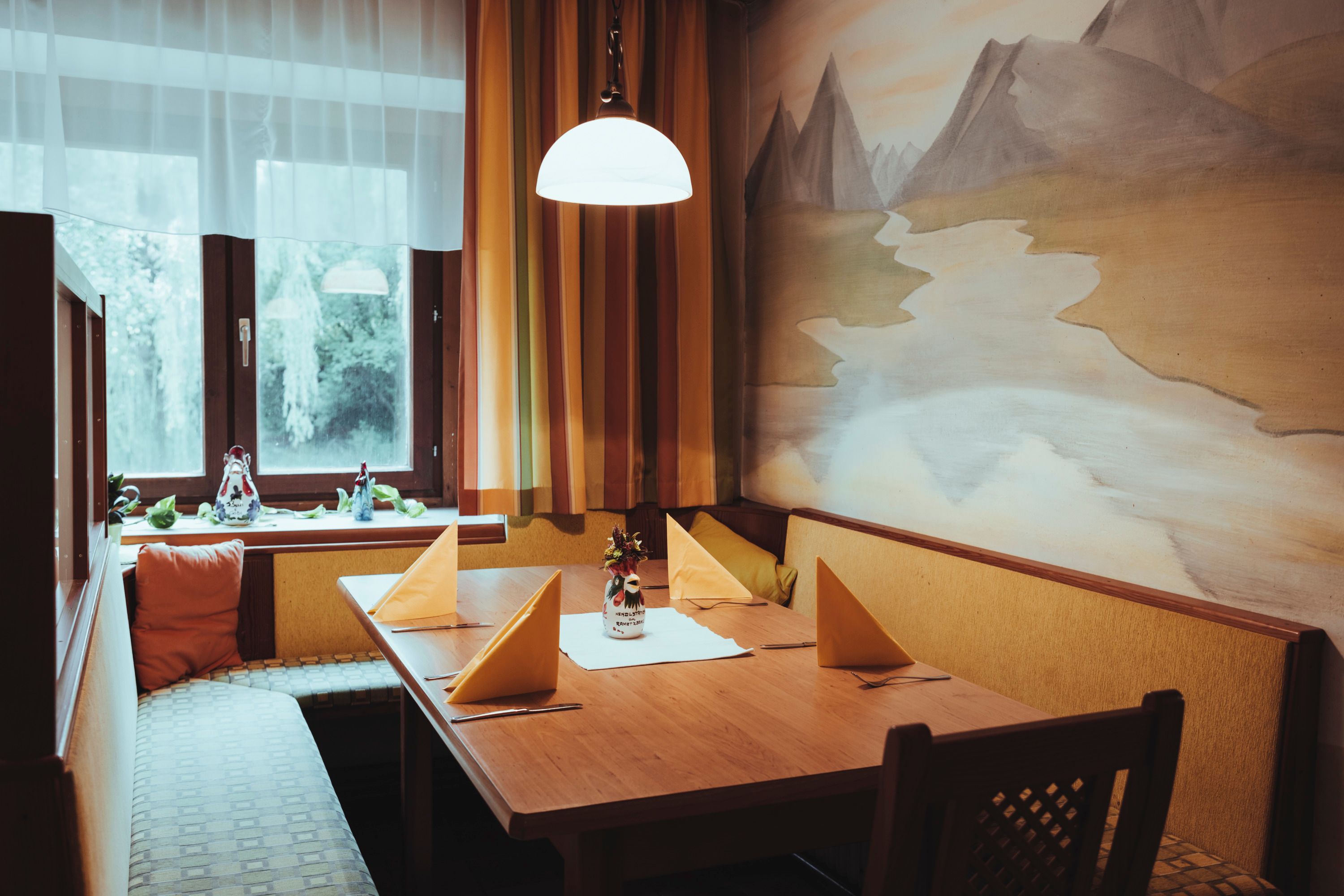 Hangulatos ülőhely fából készült asztallal, sárga szalvétákkal és falfestéssel egy étteremben.