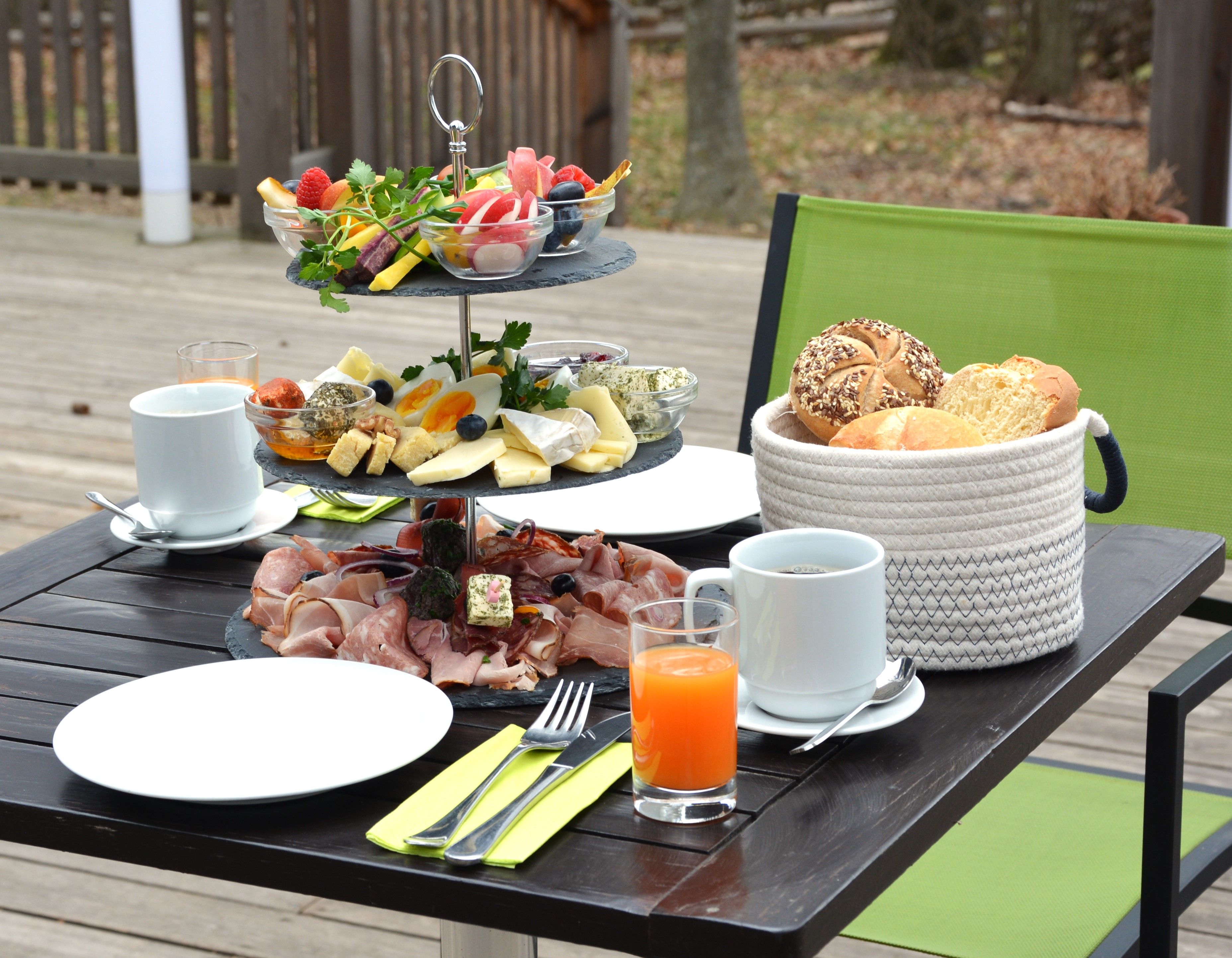 Kinti reggelizőasztal felvágottal, sajttal és zöldségekkel. Mellette tányérok, evőeszközök, italok és kenyérkosár.