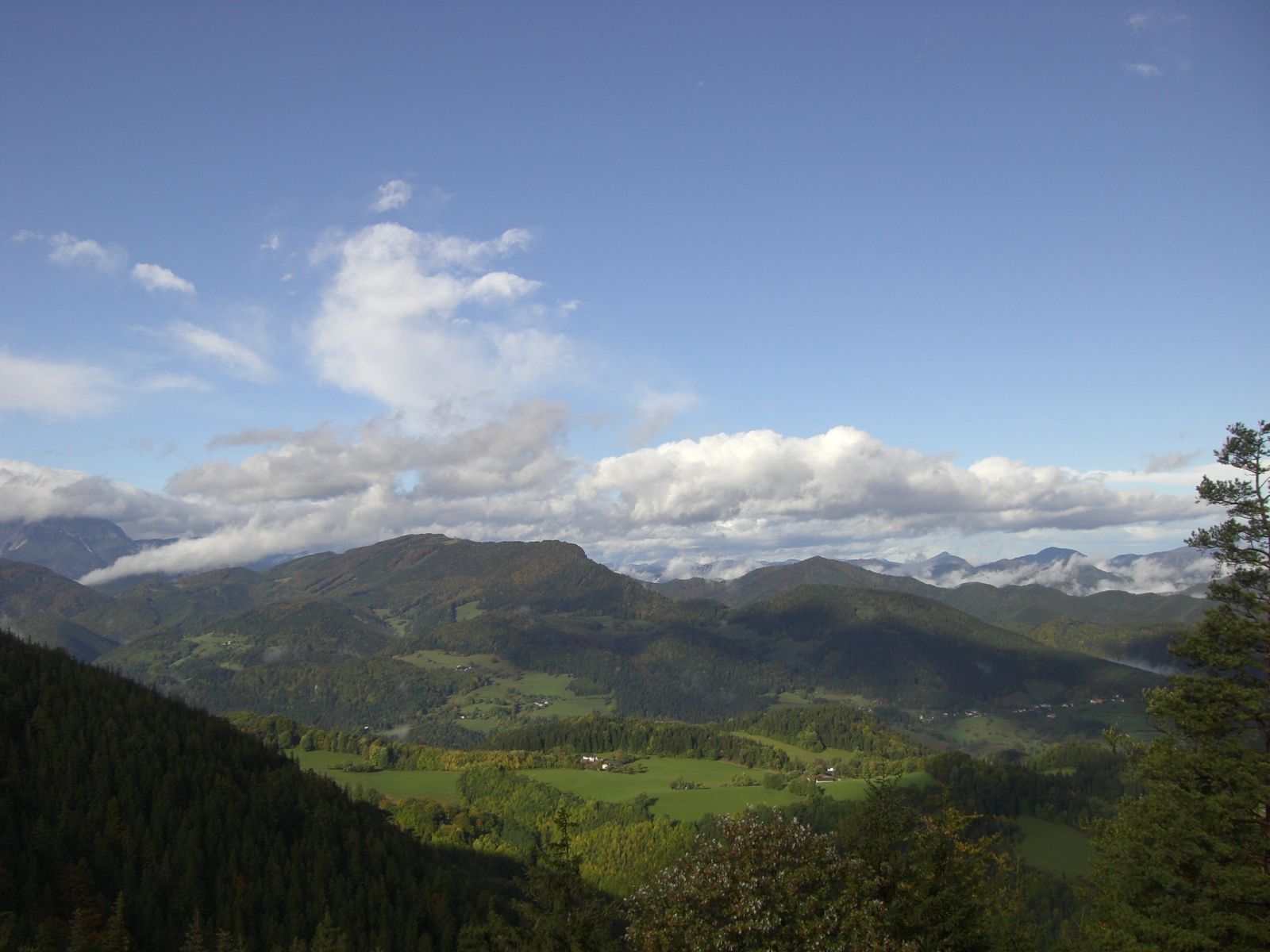 Zöld hegyvidéki táj panorámaképe kék felhős ég alatt.
