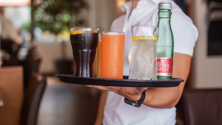 Egy mosolyg&oacute;s pinc&eacute;rnő t&aacute;lc&aacute;n k&iacute;n&aacute;lja az italokat egy hangulatos &eacute;tteremben.