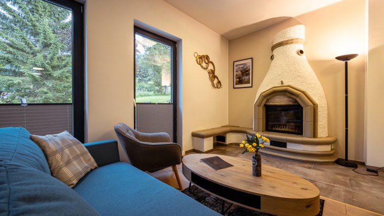 Hangulatos nappali kandallóval, kanapéval, karosszékkel és dohányzóasztallal. Nagy ablakok, kilátással a zöldövezetre.