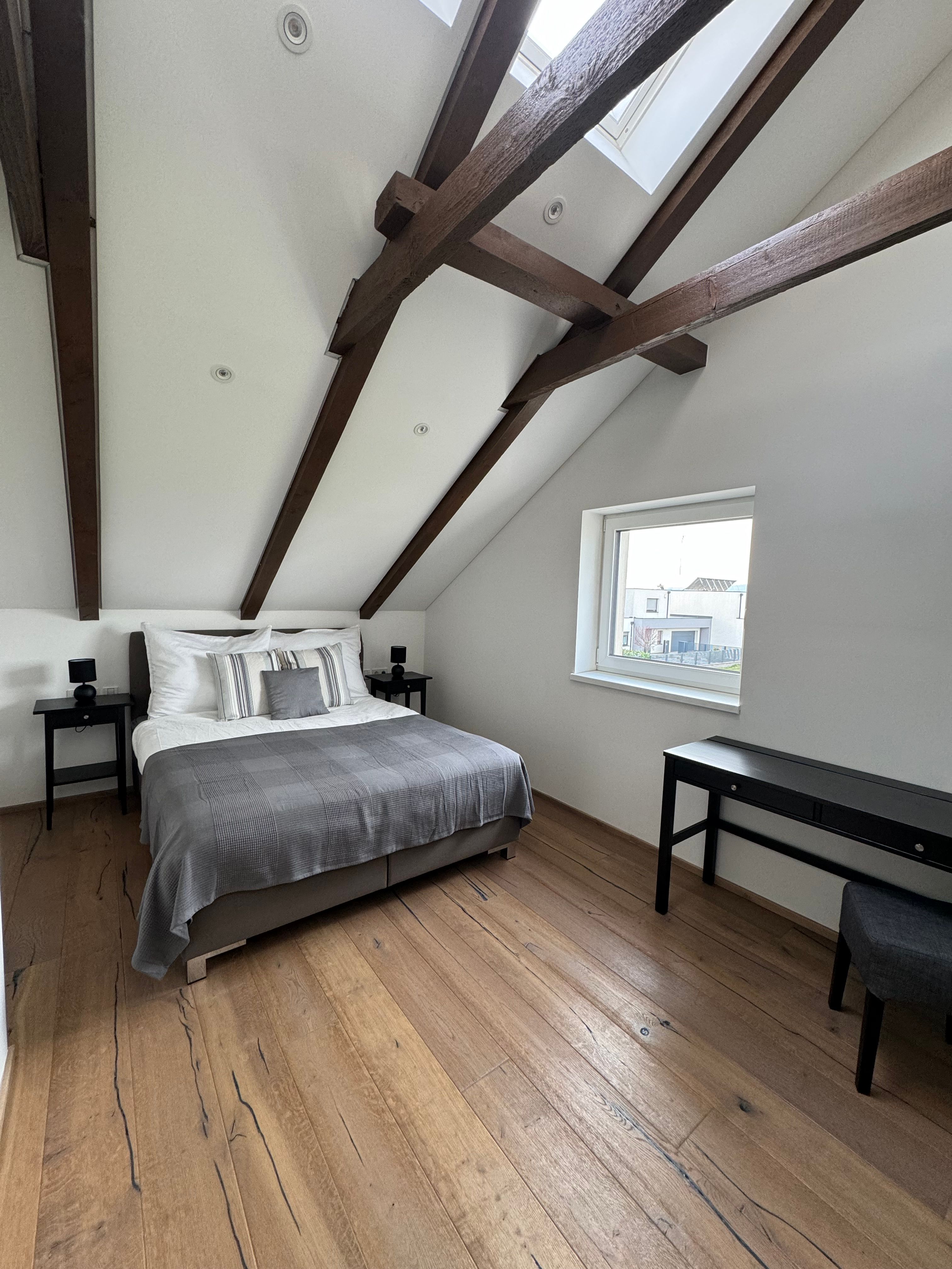 Modern hálószoba fagerendás mennyezettel, franciaággyal, fapadlóval és ablakkal.