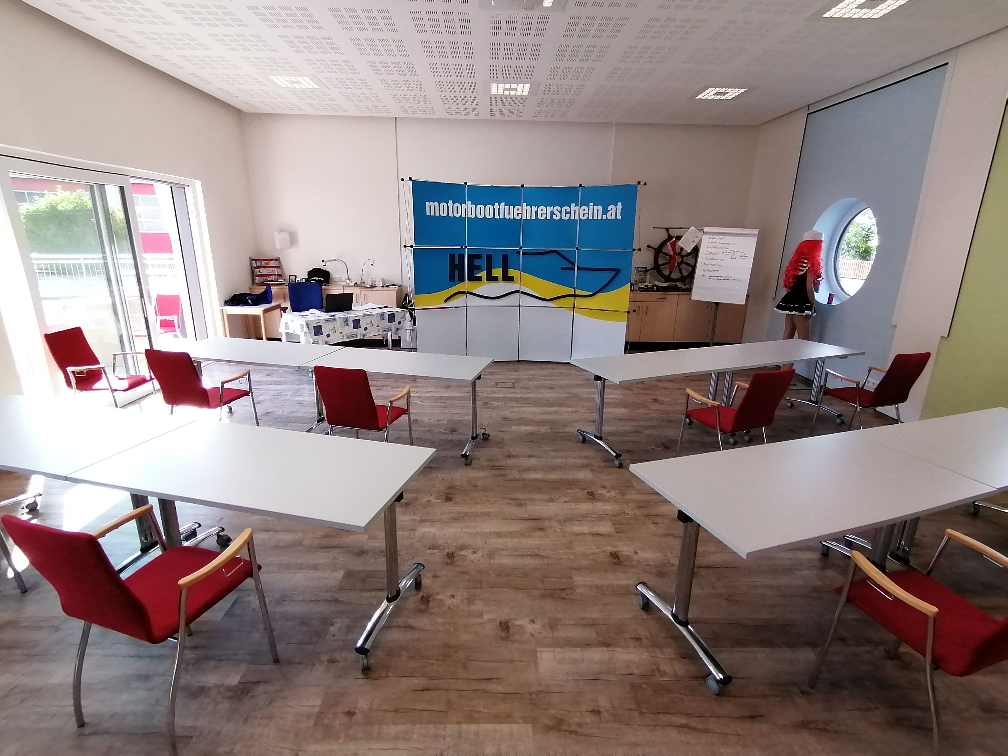 Oktatóterem asztalokkal és székekkel, Hell skipper school bannerrel, flipcharttal és próbababával.