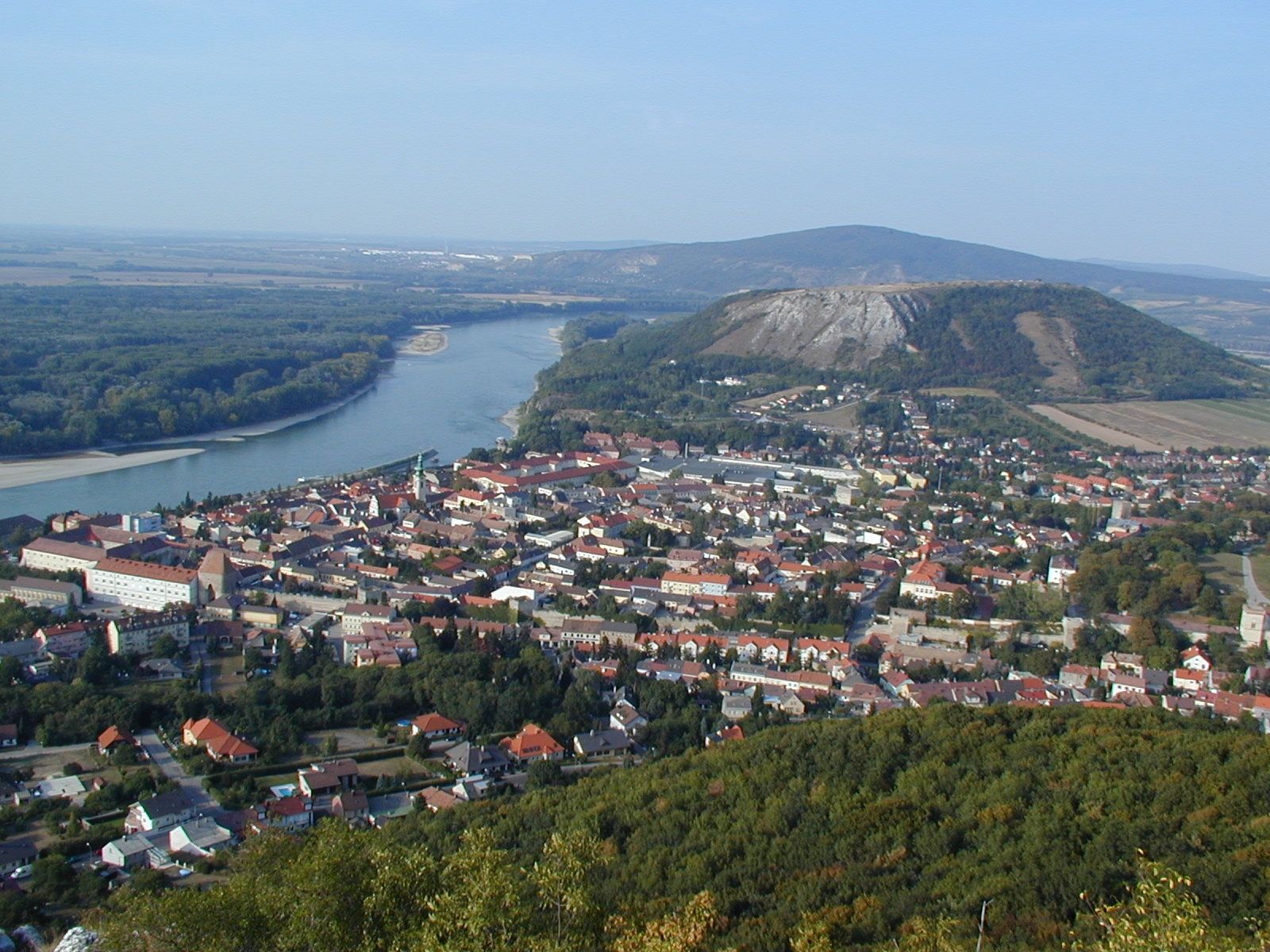 Egy város panorámaképe, a háttérben folyó és dombok.