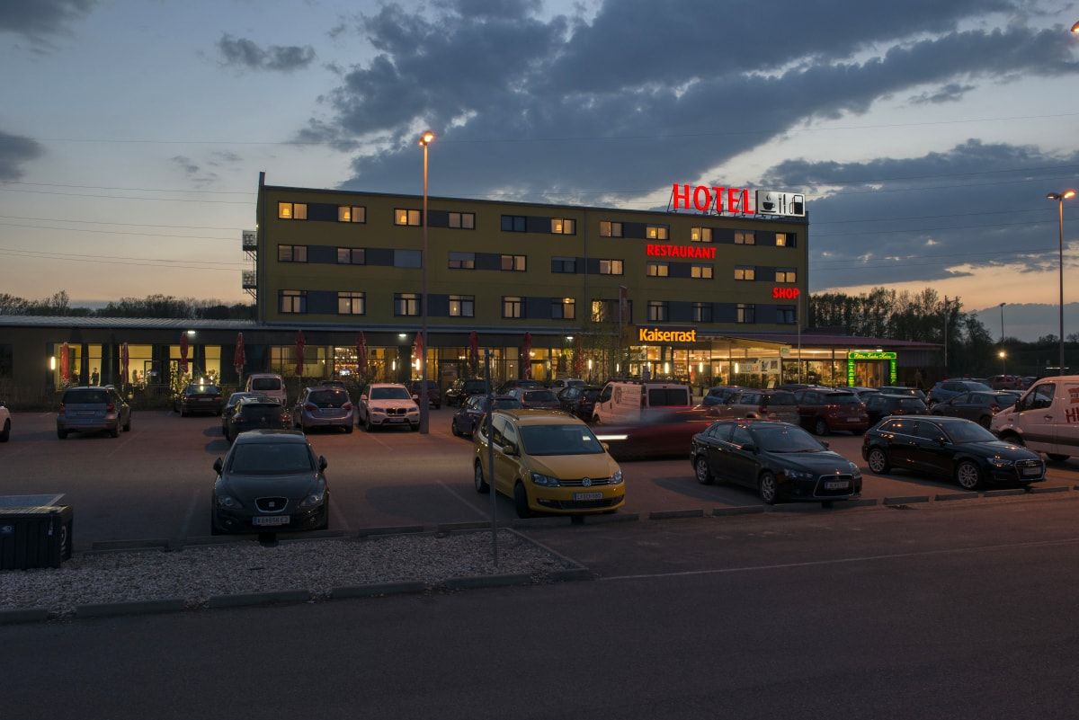 Esti felvétel egy szállodáról, parkolóval és autókkal előtte.