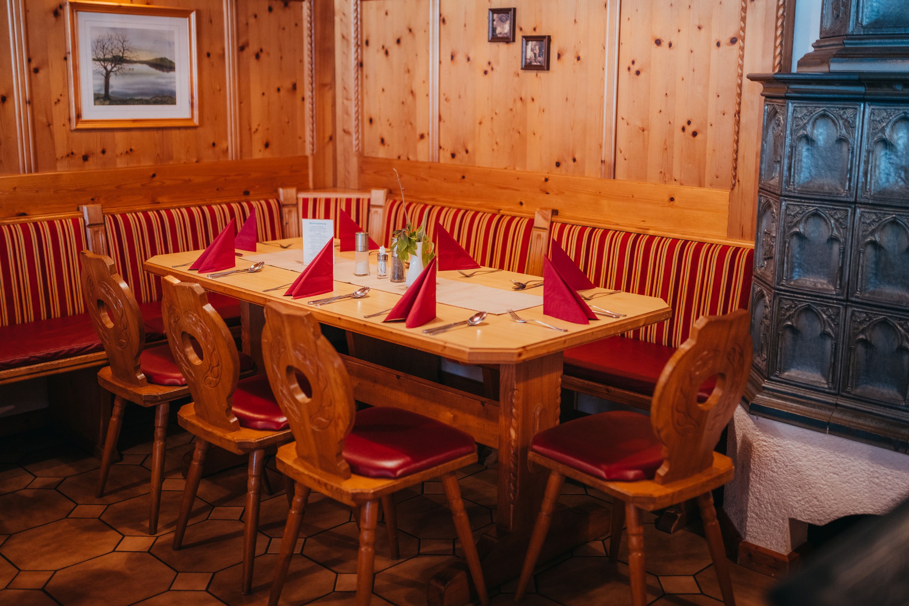 Hangulatos szalon fabútorokkal, piros kárpitozással és cserépkályhával.