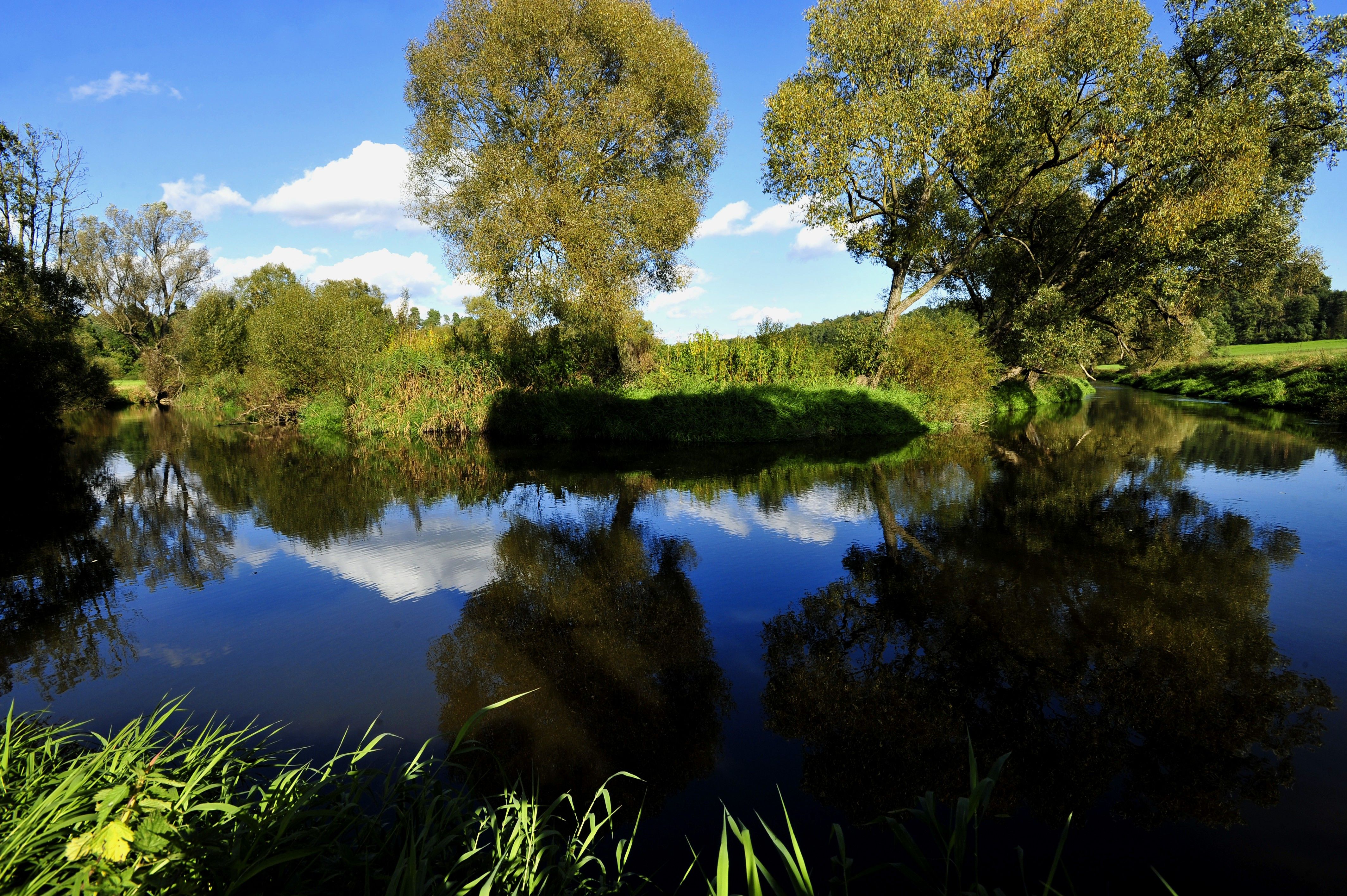 Nyugodt folyó a Dobersberg natúrparkban, a háttérben fák és kék égbolt.