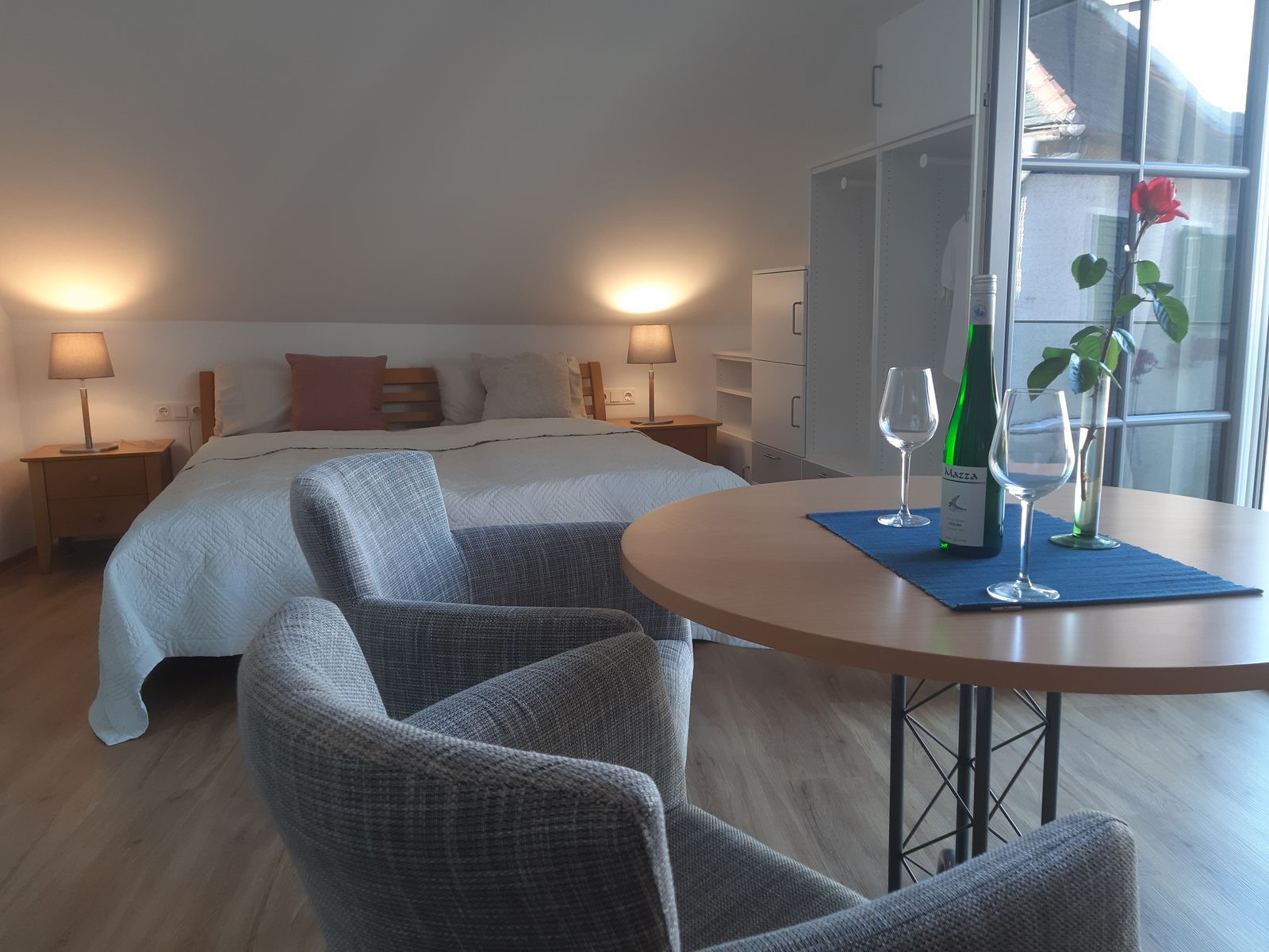 Hangulatos hálószoba franciaággyal, asztallal, két székkel, borosüveggel és poharakkal.