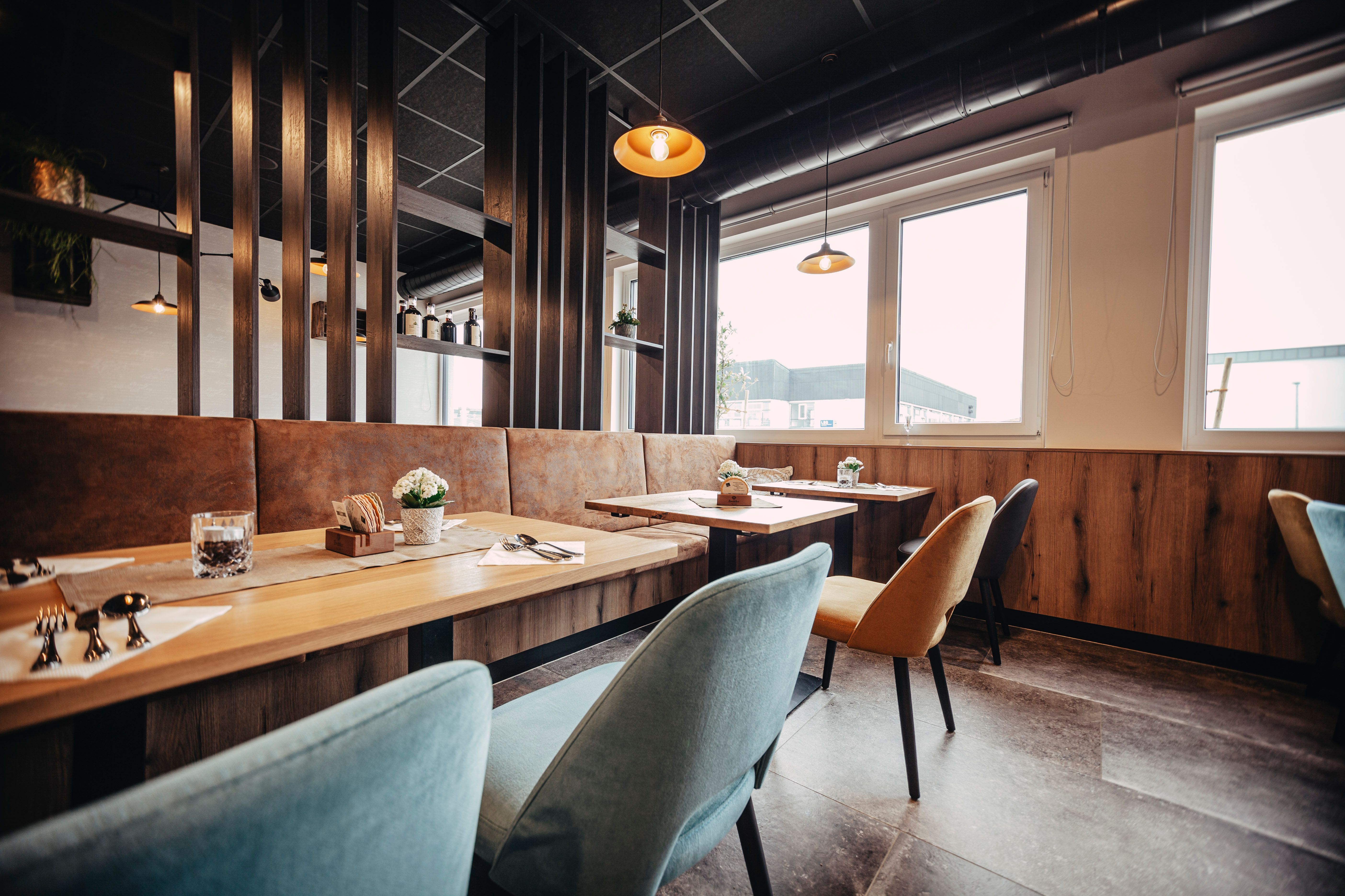 Modern étterem faasztalokkal, színes székekkel és nagy ablakokkal.