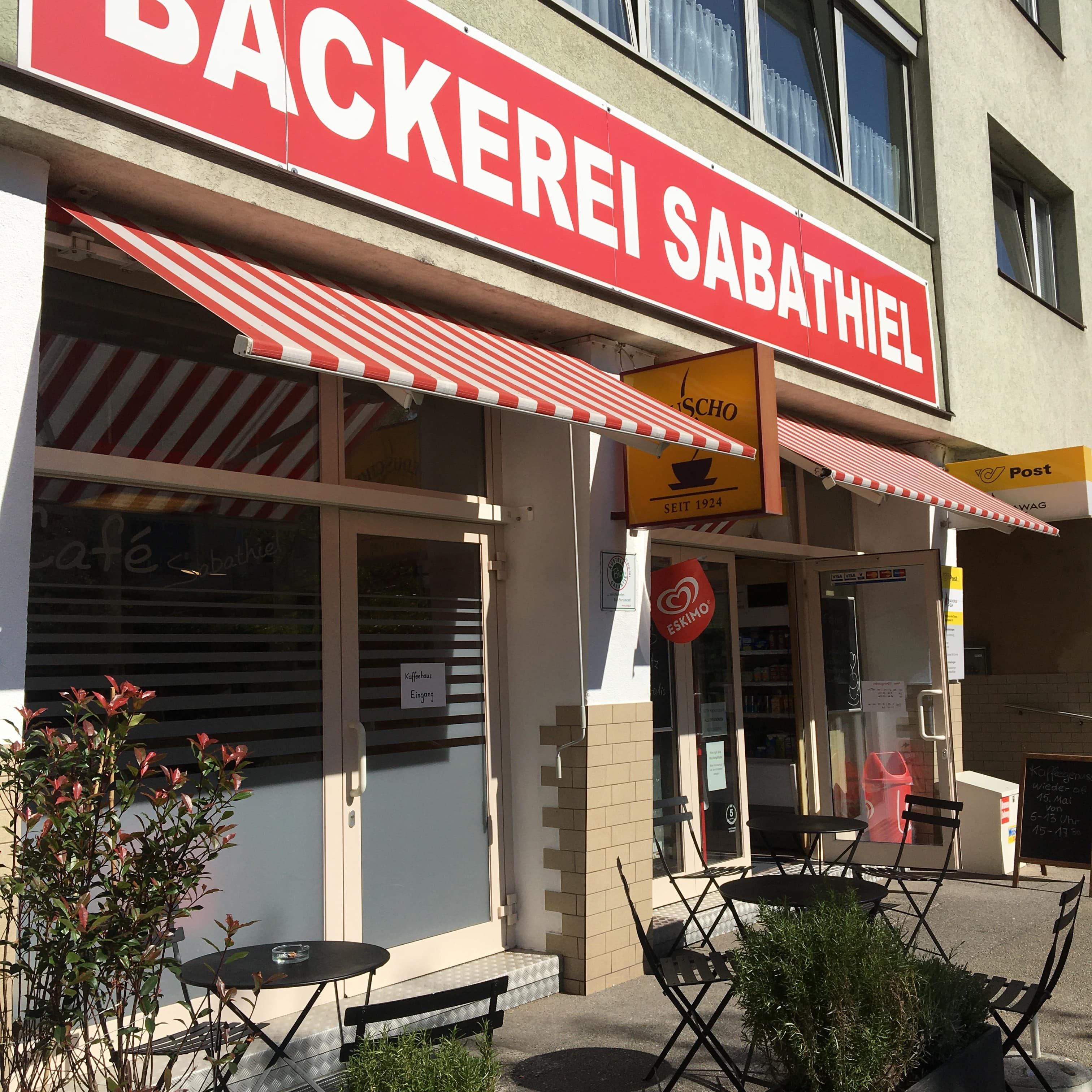 Egy pékség külső nézete piros napellenzővel és szabadtéri ülőhelyekkel.
